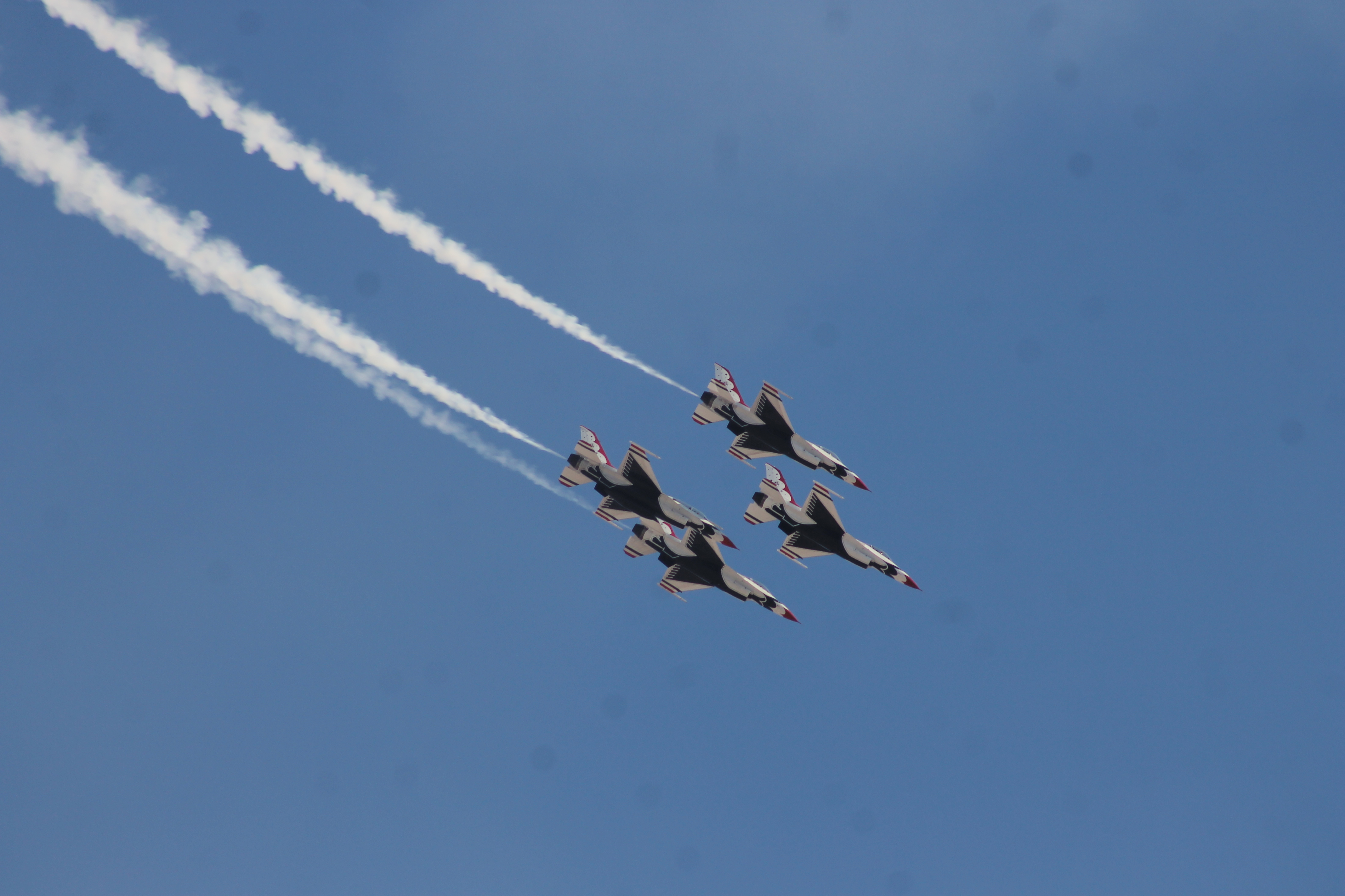 Four red, white, and blue jets in tight diamond formation against a clear blue sky.