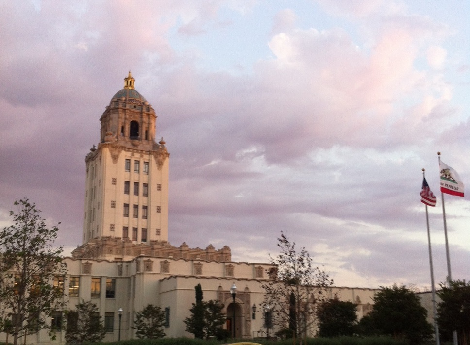 Beverly Hills City Hall domed tower at dusk with US and California flags flying in front.