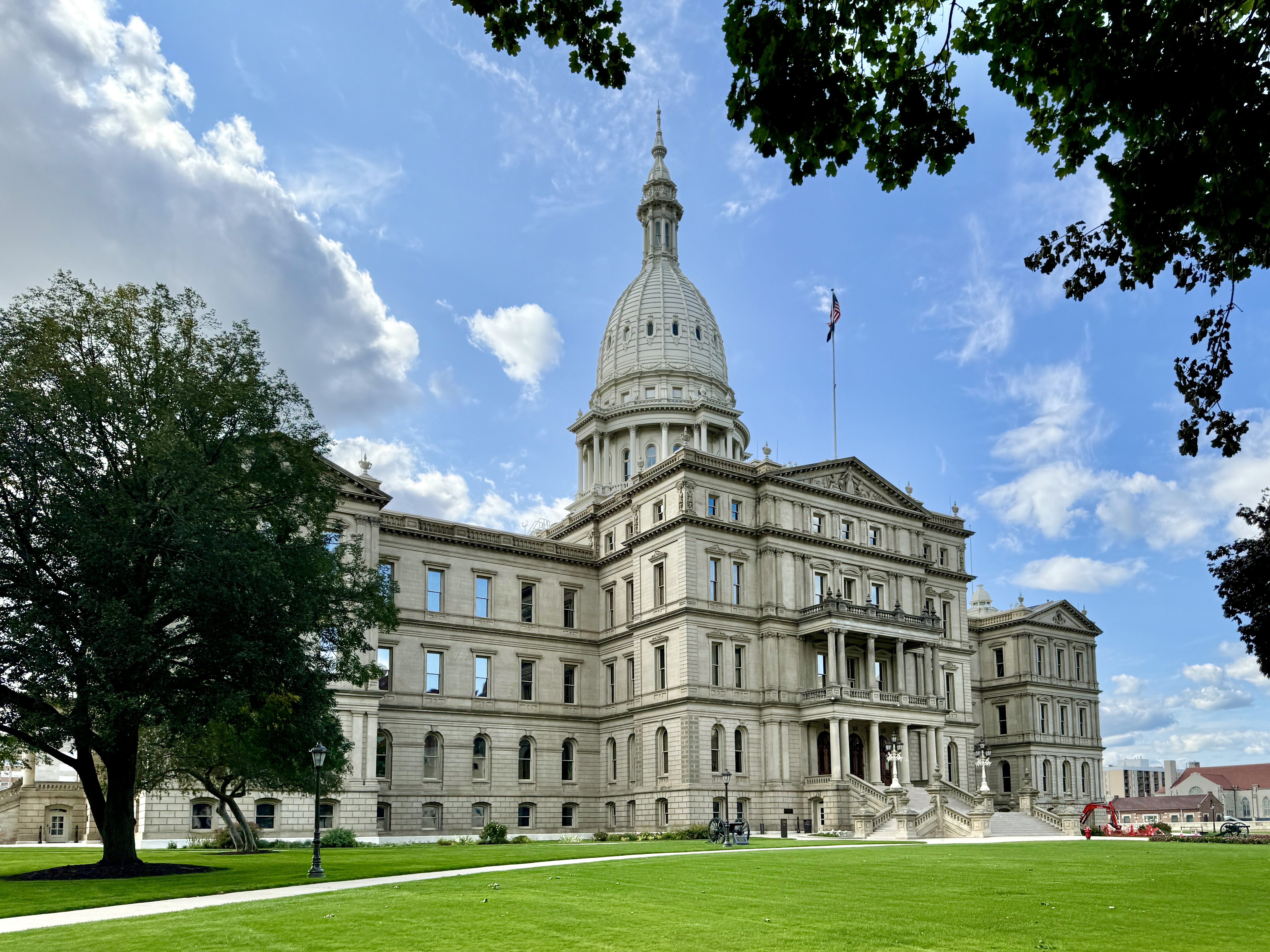 Michigan State Capitol building with limestone facade and central dome, surrounded by trees on a sunny day.