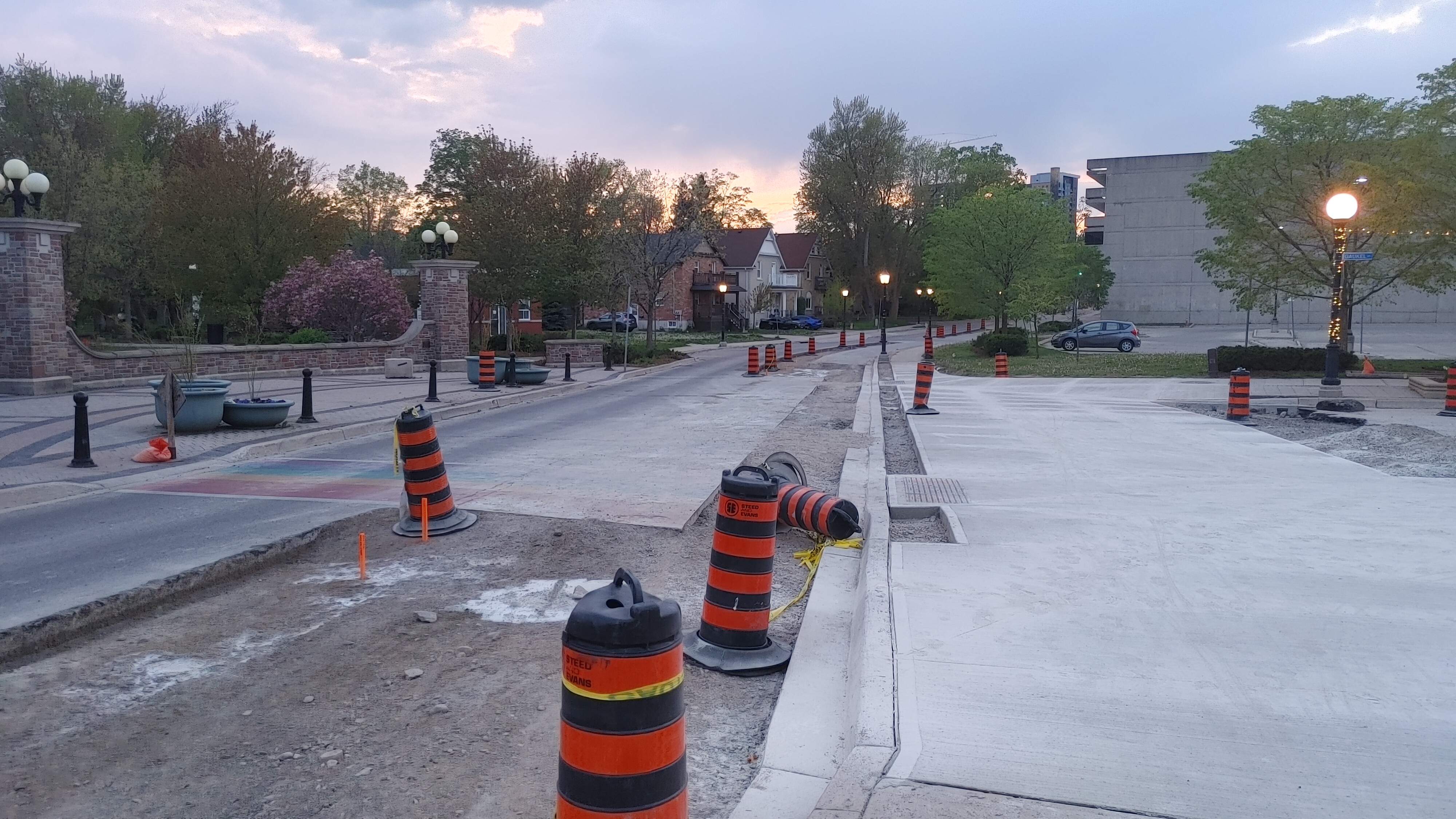 Orange construction barrels line a downtown street with freshly poured concrete curbing.