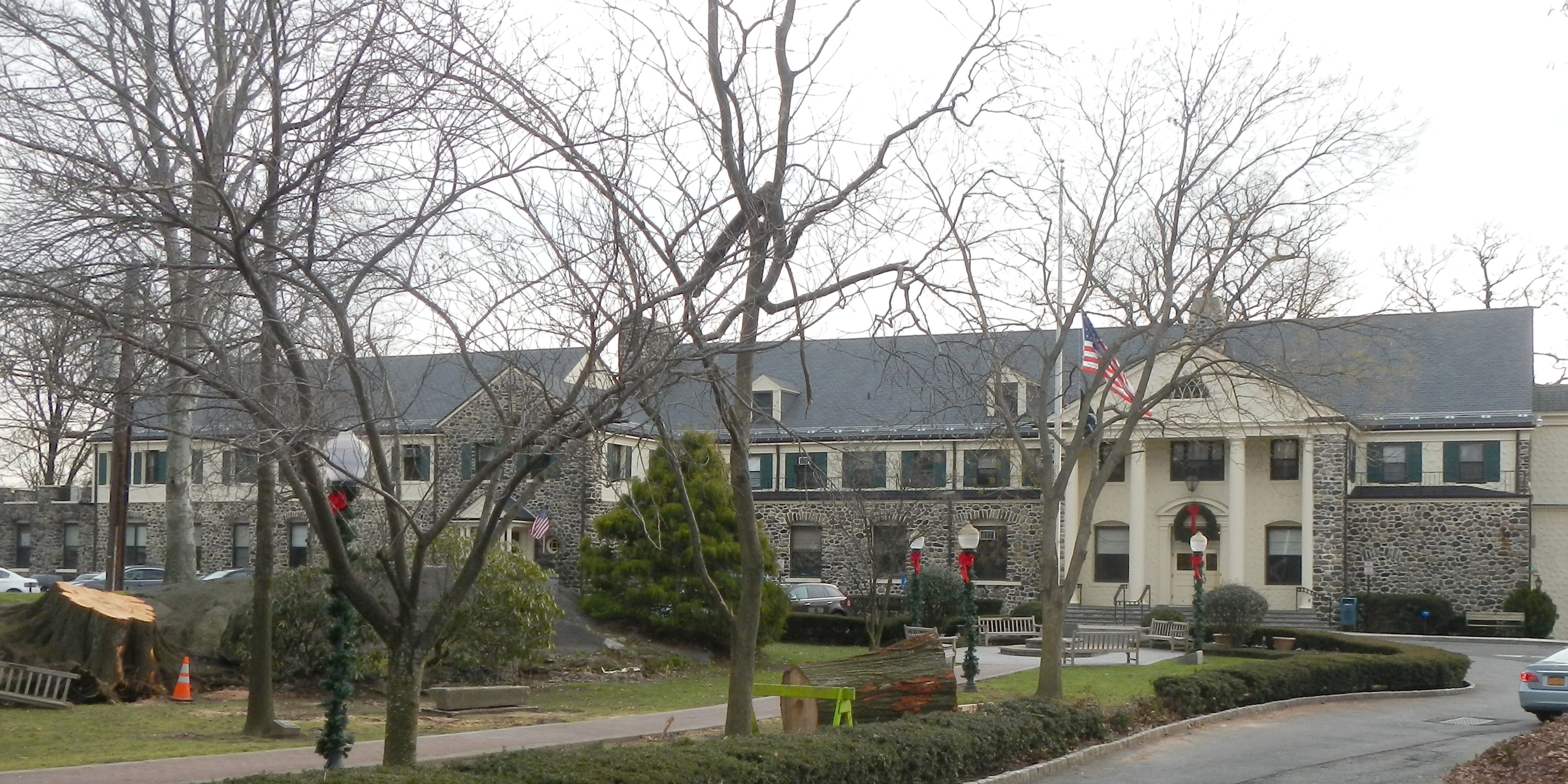 Stone municipal building with an American flag and bare trees on a cloudy day.