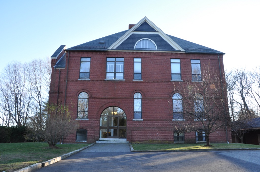 Three-story red brick school building with arched entrance and bare surrounding trees.