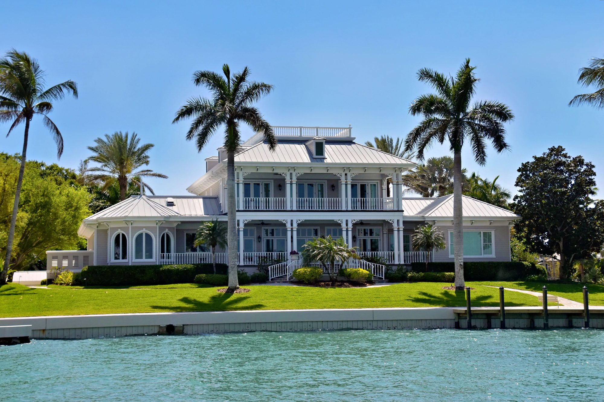 Elegant waterfront villa with palm trees and lush greenery, ideal for luxury living.