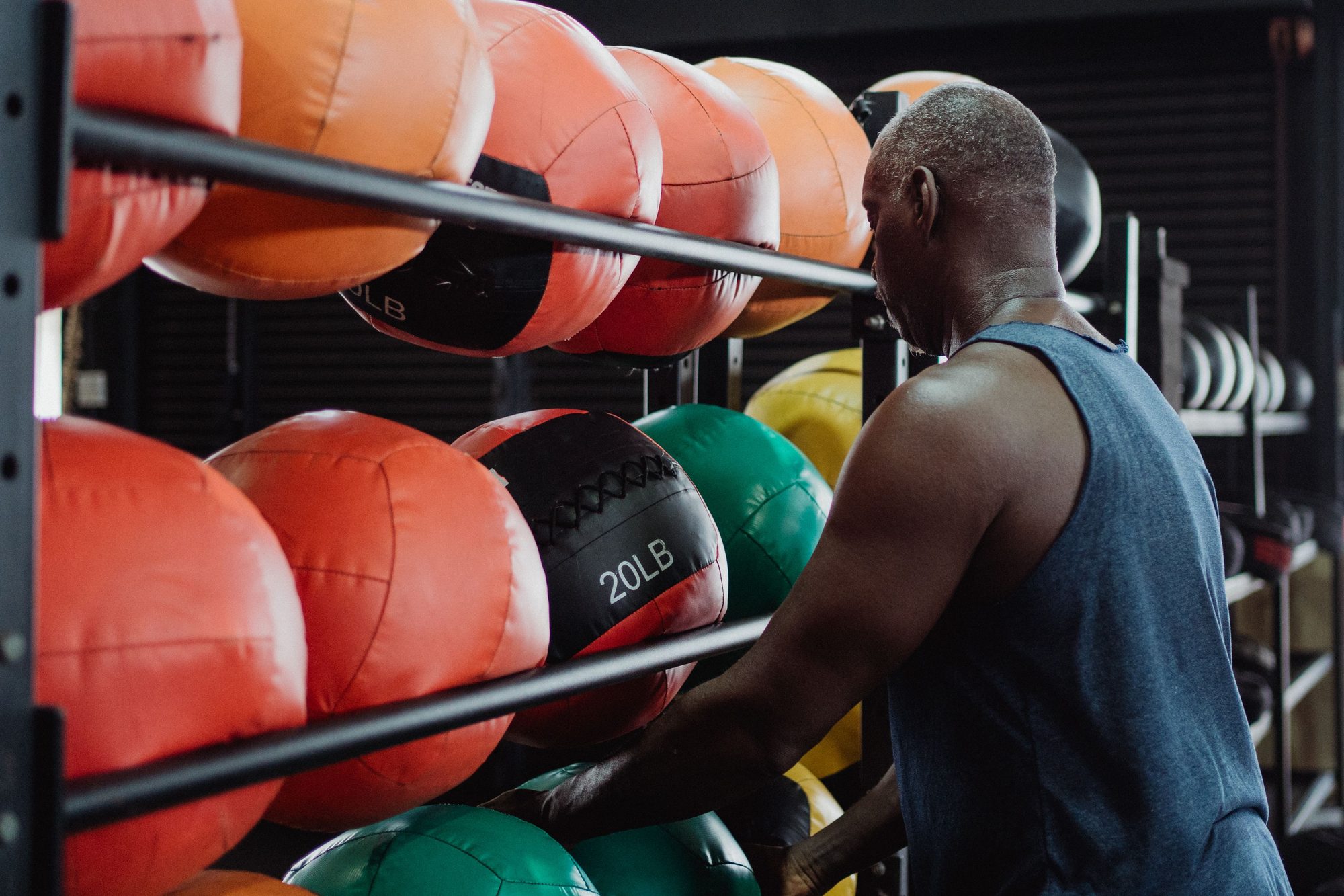 Athletic man selecting a 20-pound medicine ball for his fitness routine in a modern gym setting.