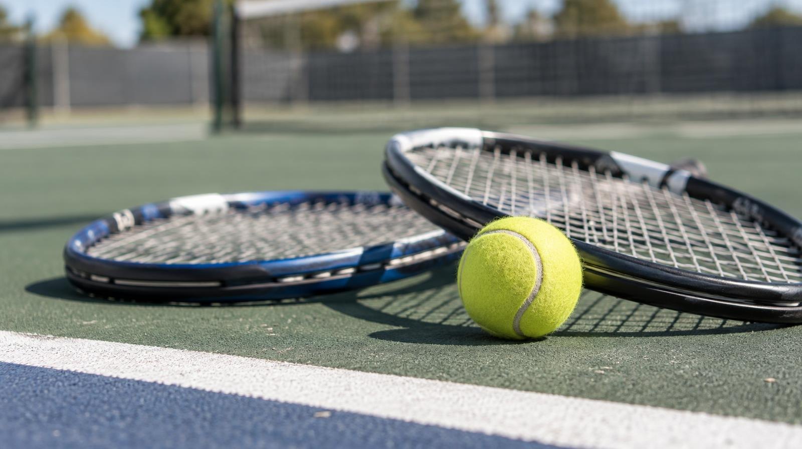 Two tennis rackets and a yellow ball resting on a hard court surface.