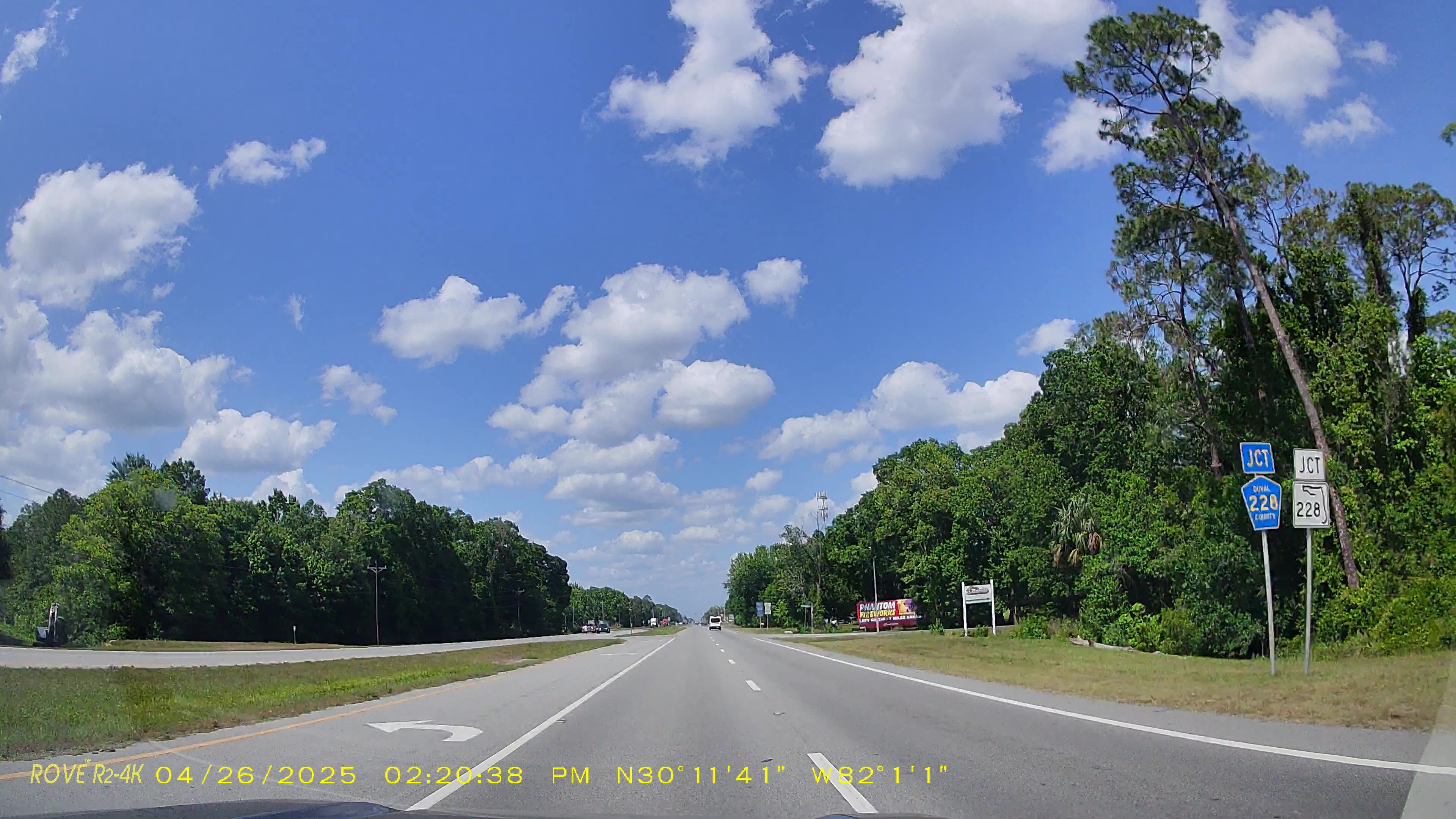Dashcam view of a two-lane highway with road junction signs and trees on both sides.