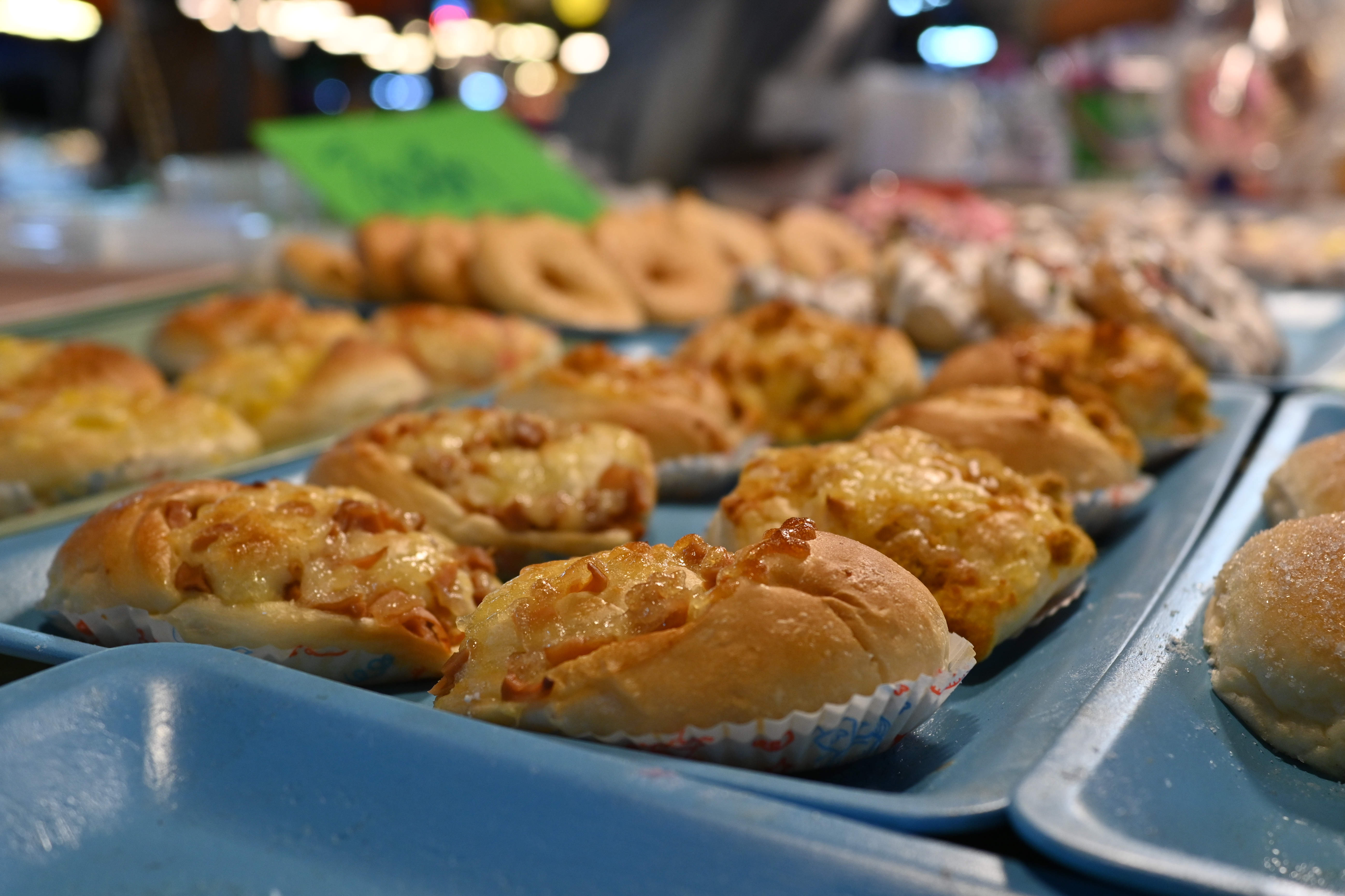 Golden-brown glazed buns arranged on blue metal trays with paper liners.