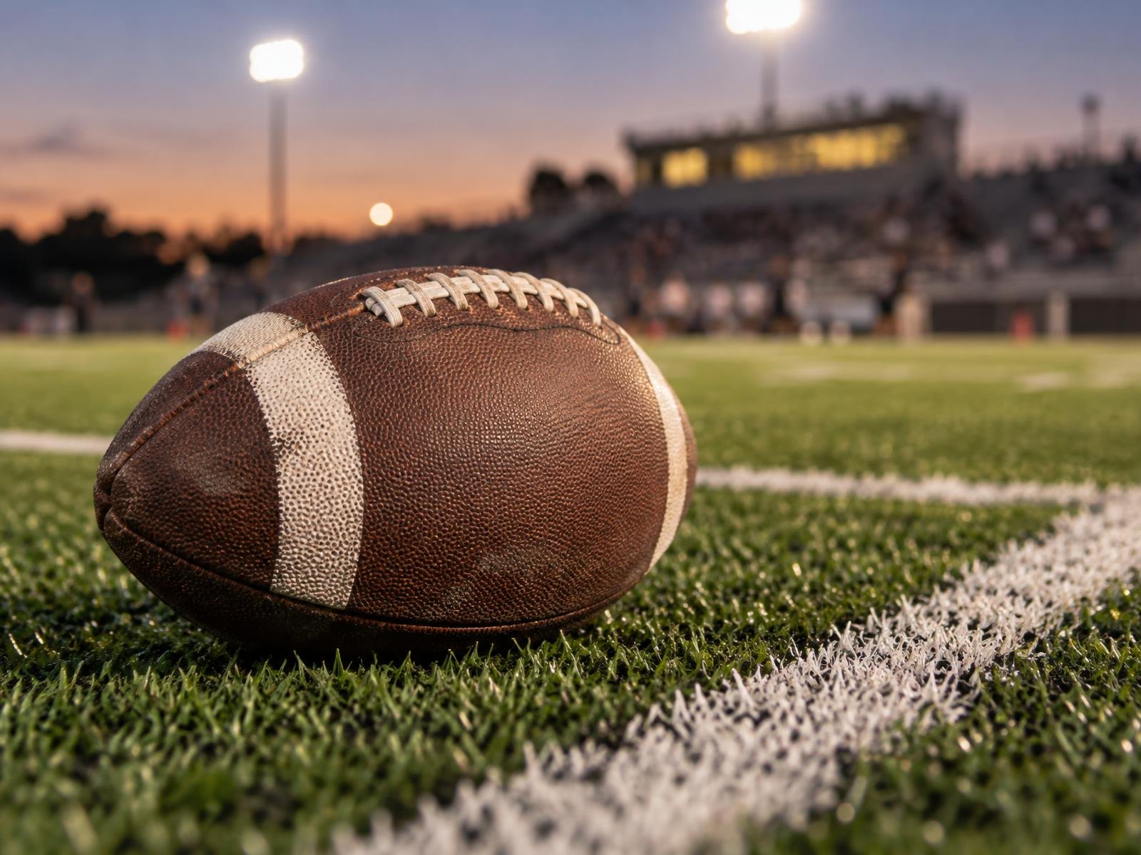 An American football resting on green artificial turf beside a white yard line.
