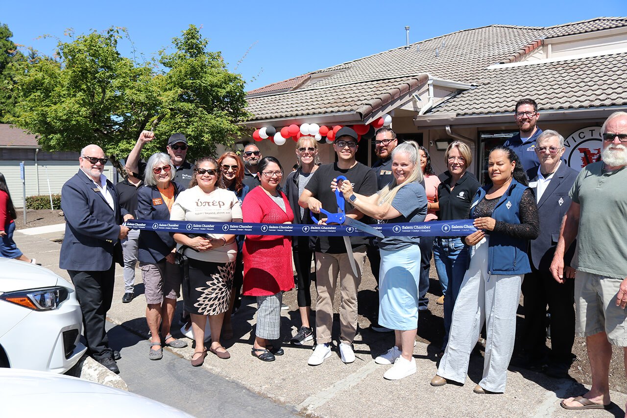 Group of people cutting a blue ribbon at an outdoor ribbon-cutting ceremony.