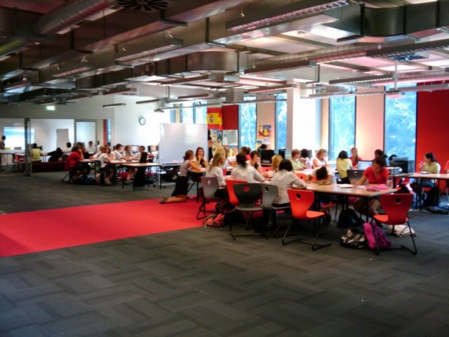Students seated at tables in a large open-plan high school learning space.