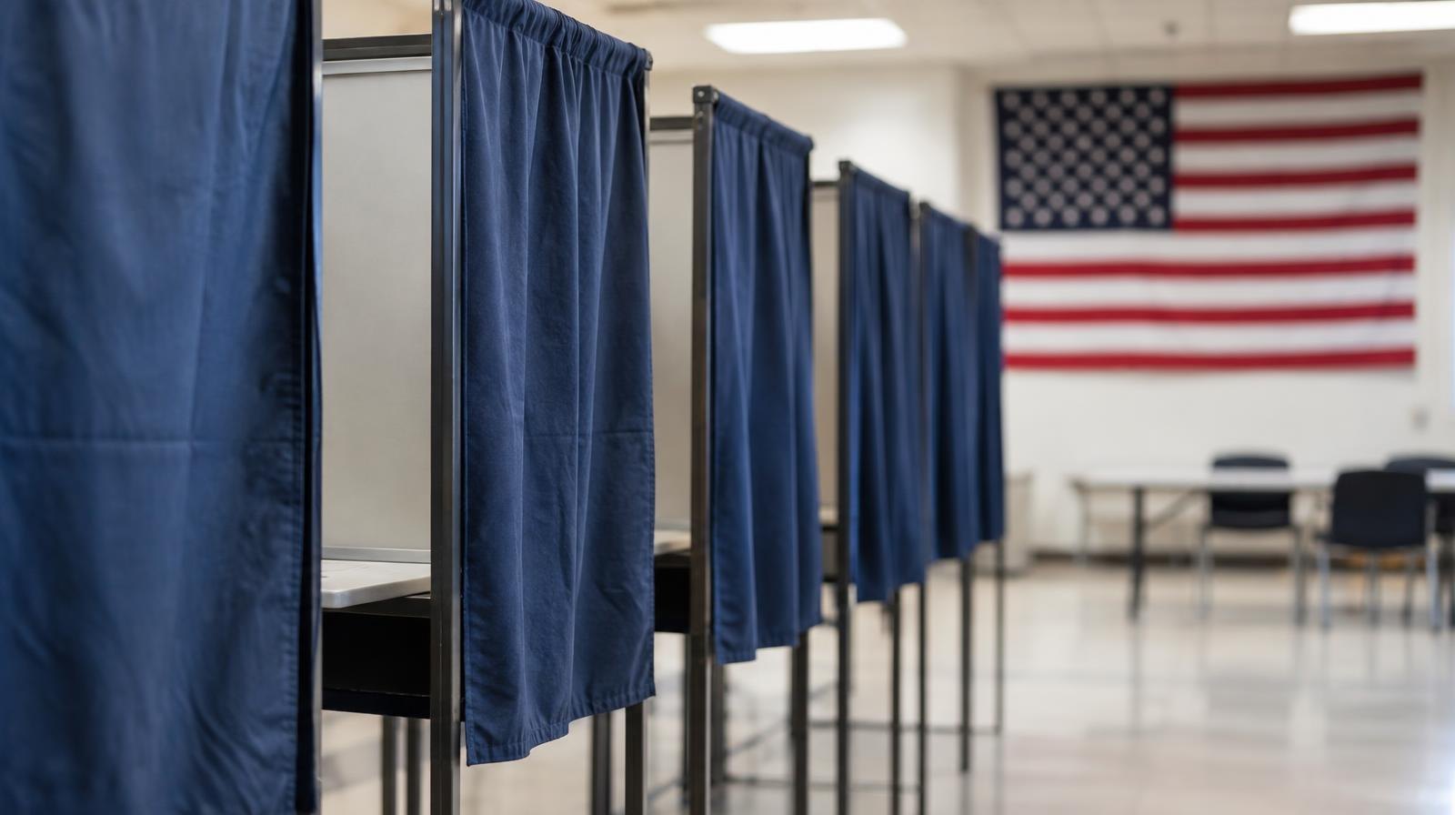 A row of empty privacy voting booths with curtains in a polling place.