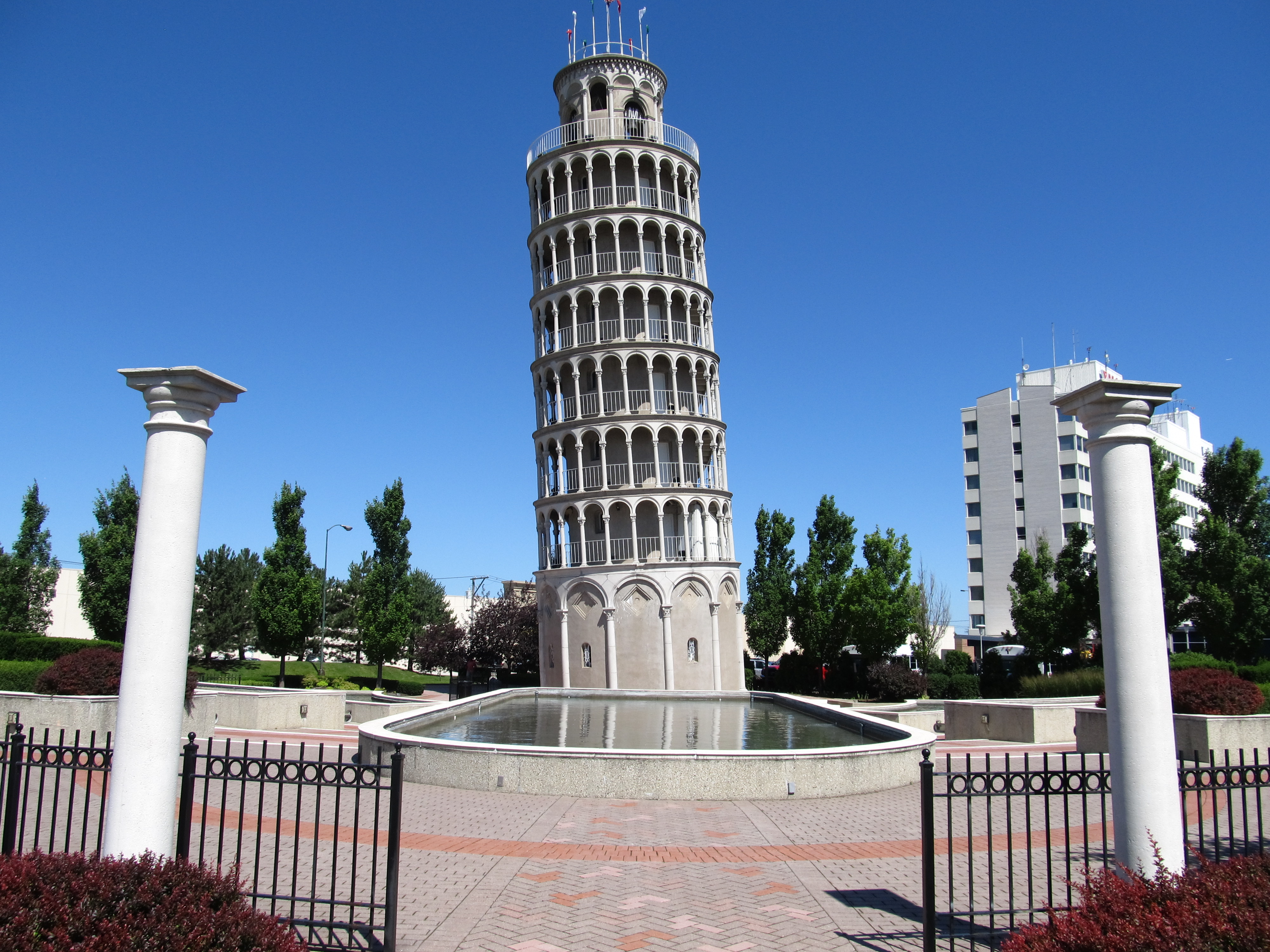 Leaning tower replica with a fountain, decorative columns, and iron fencing in the foreground.