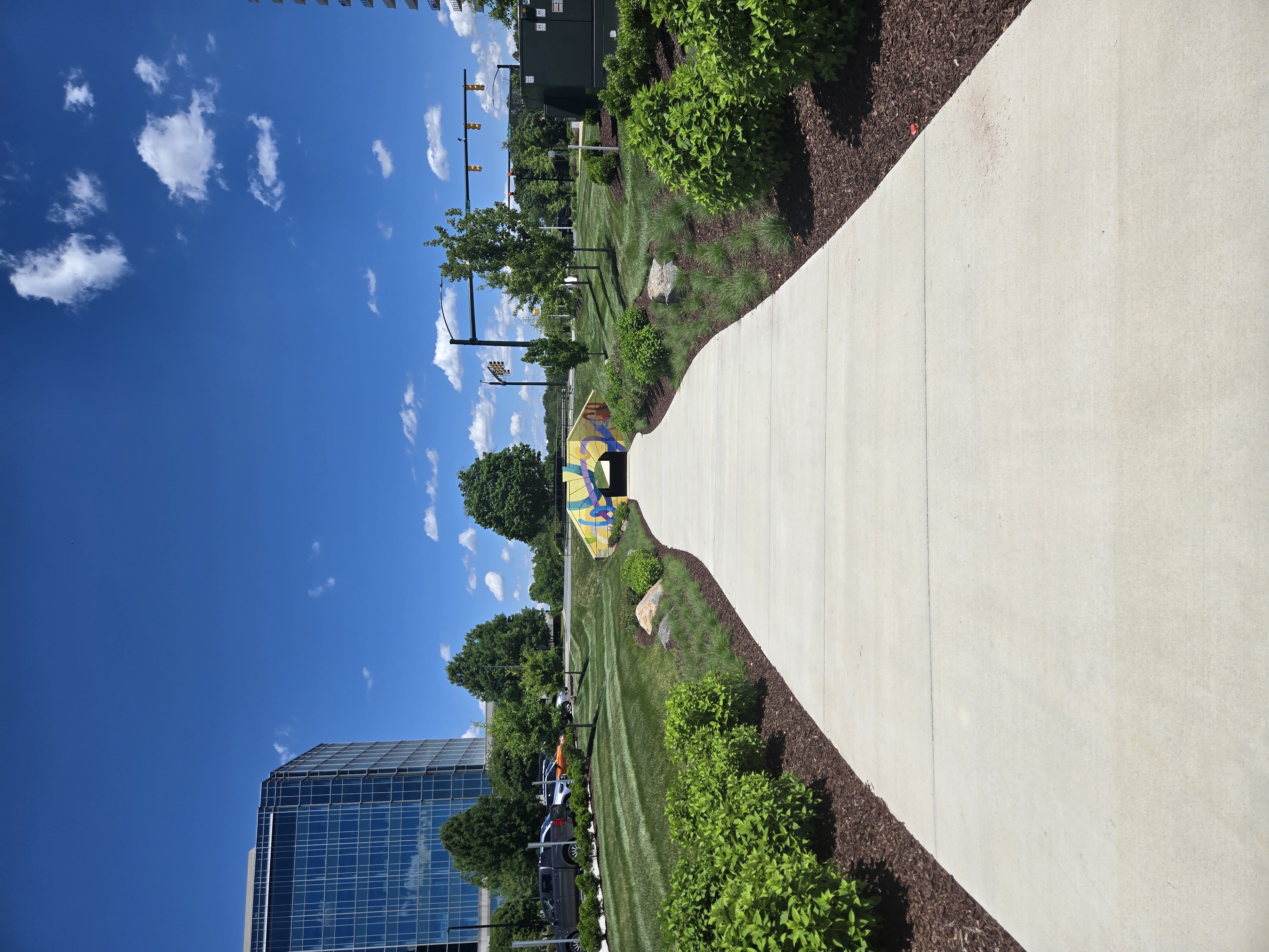 Landscaped walkway with a colorful arch and glass office building at a corporate park.