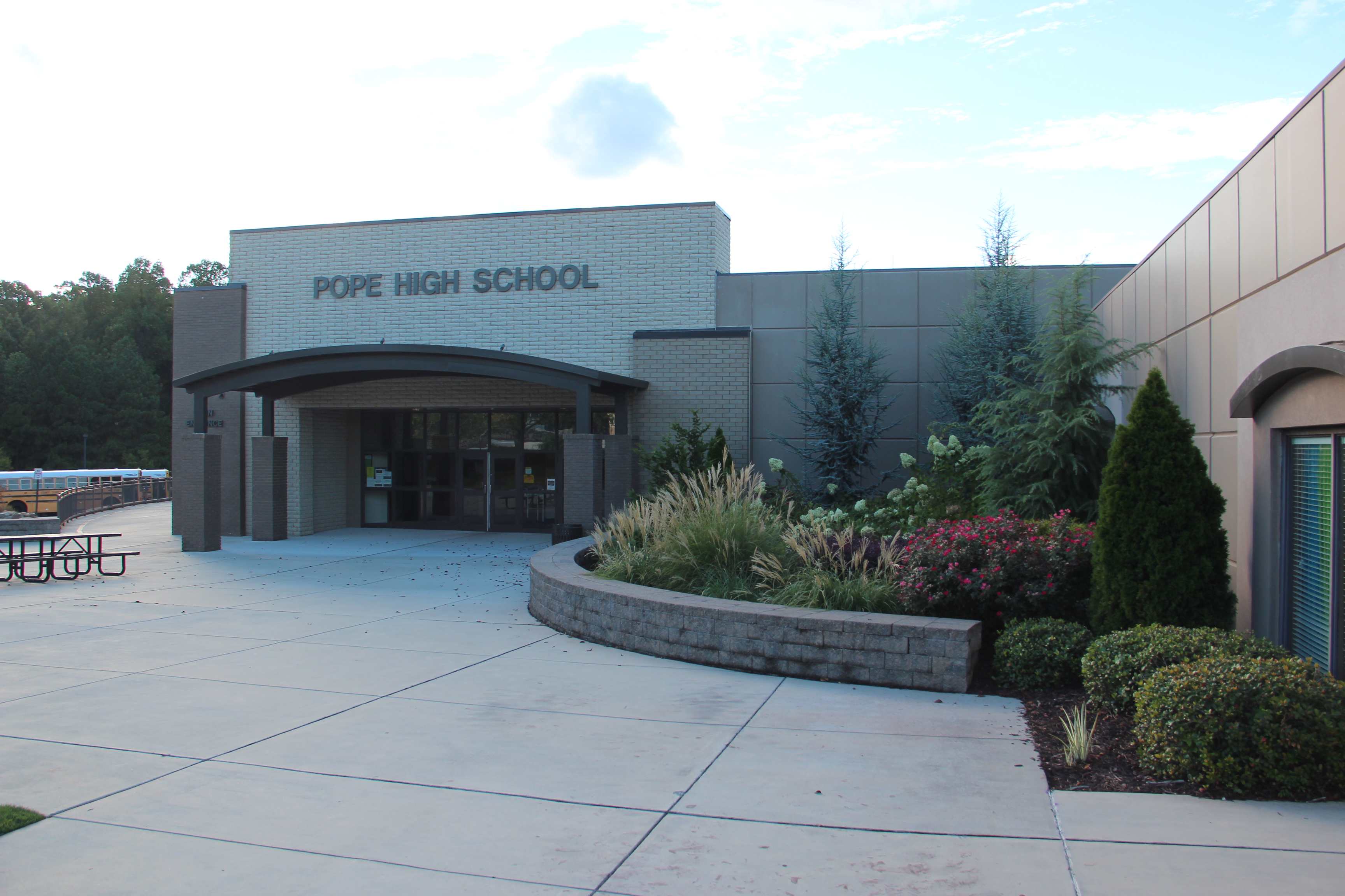 Front entrance of Pope High School, a brick building with landscaped grounds and school buses visible.