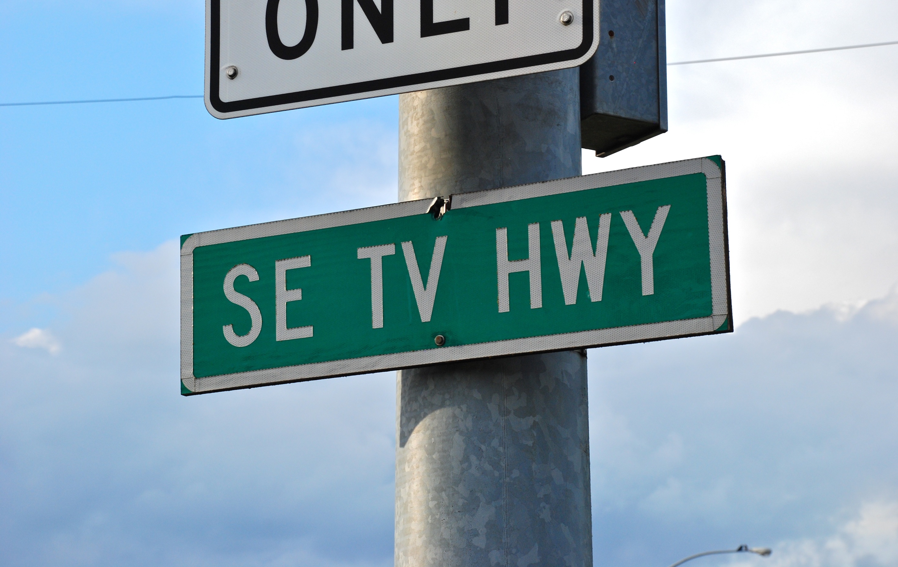Green street sign reading SE TV HWY mounted on a pole against a cloudy sky.