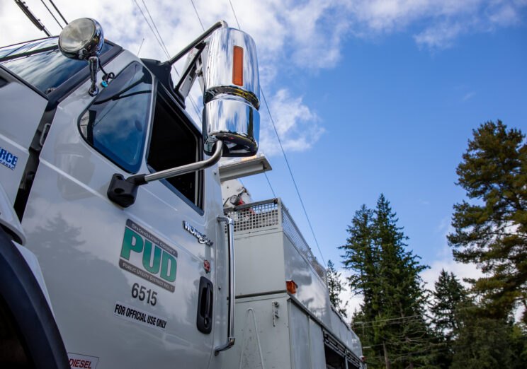Close-up of a white utility truck cab with a chrome exhaust stack against a blue sky.