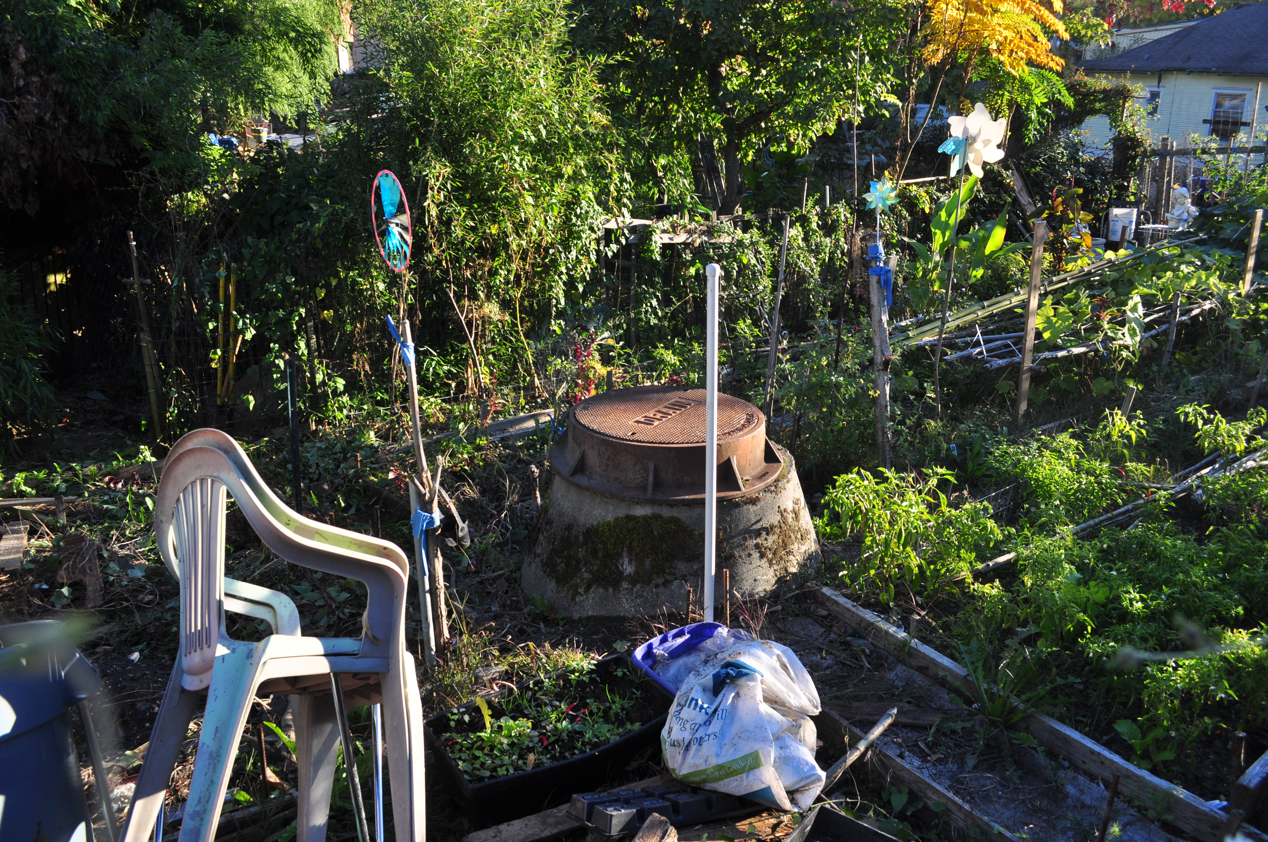 Raised planting beds with green vegetables, pinwheels on poles, and a white lawn chair in a garden.