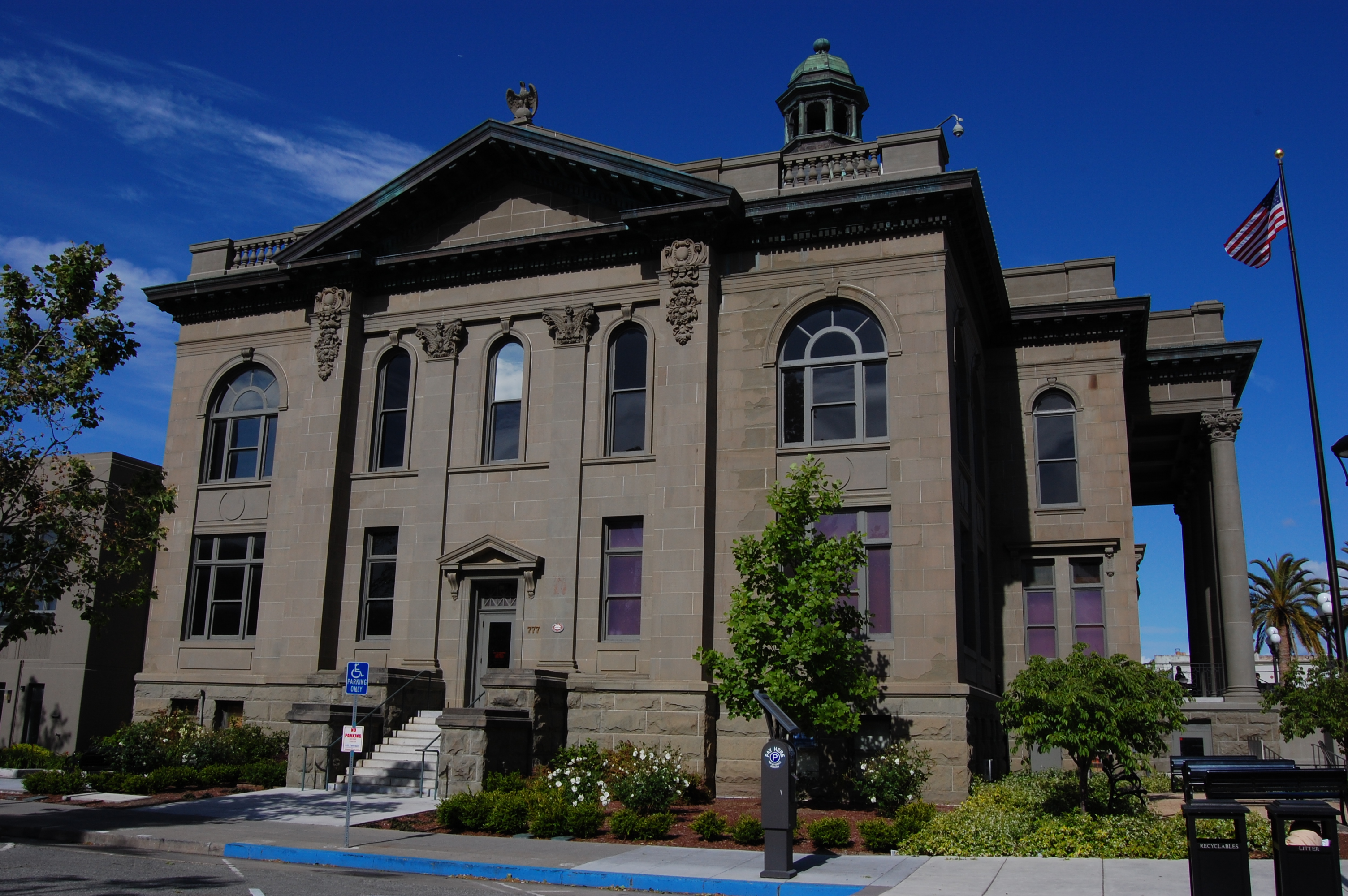 Neoclassical stone courthouse building with arched windows, copper cupola, and American flag.