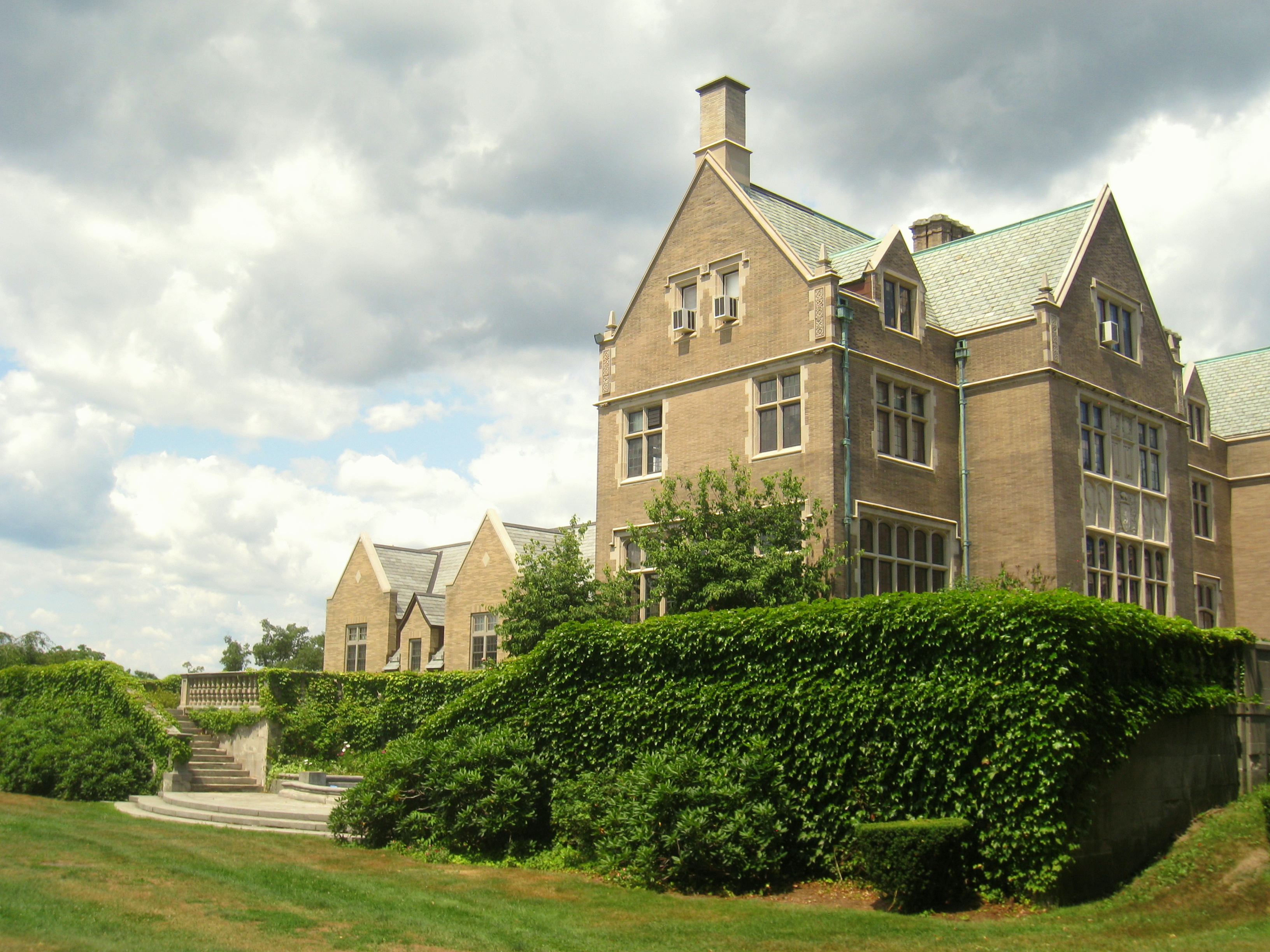 Large brick Tudor-style school building with green hedges and a stone staircase.