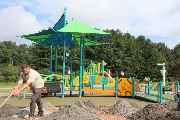 Worker bending over gravel surface in front of a colorful playground with a green shade canopy.