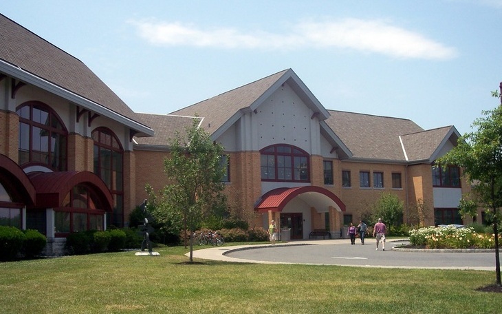 Brick public library building with red entrance canopy and landscaped grounds.