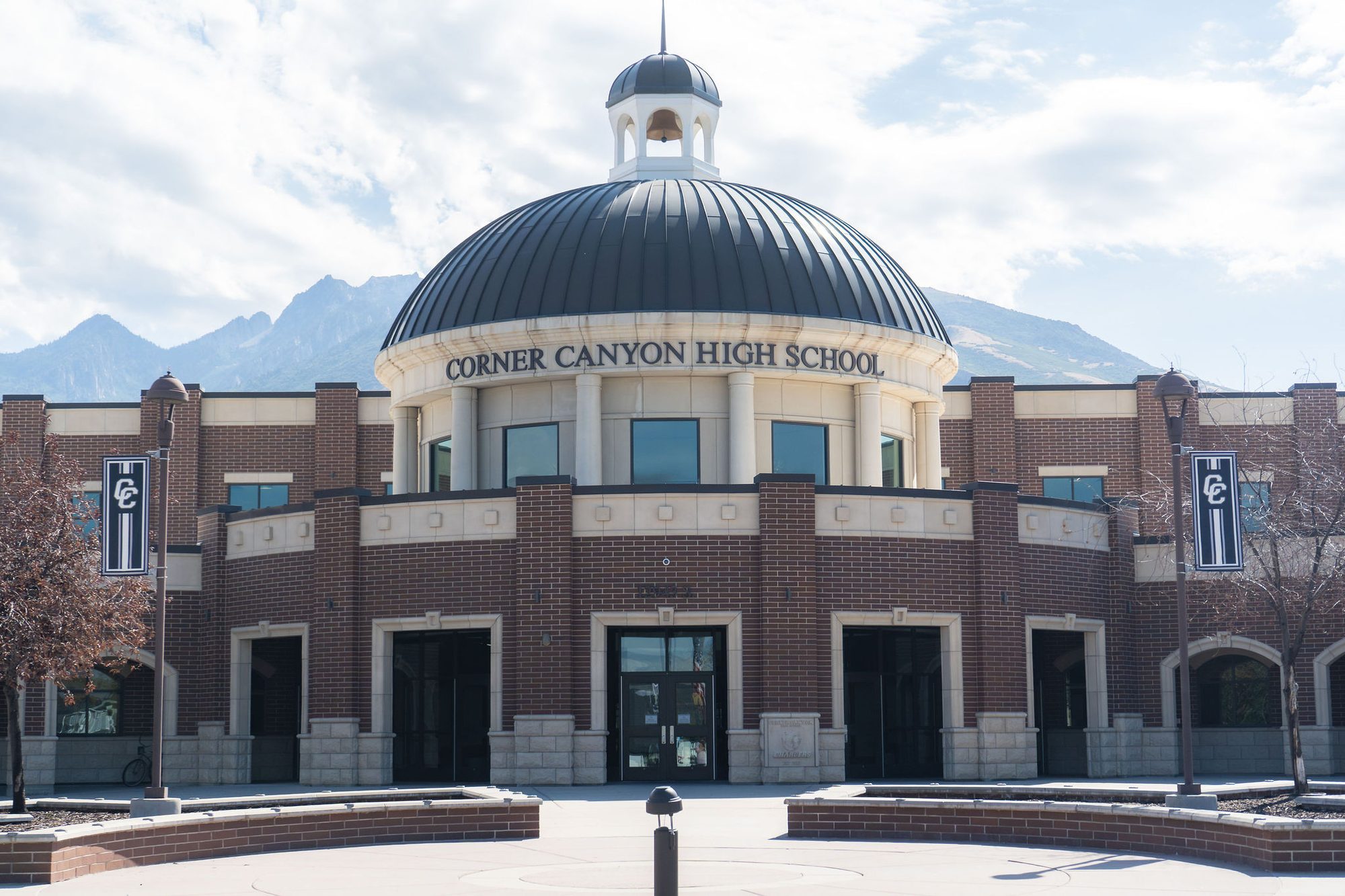 Brick high school building with a large dome and cupola, mountains in the background.