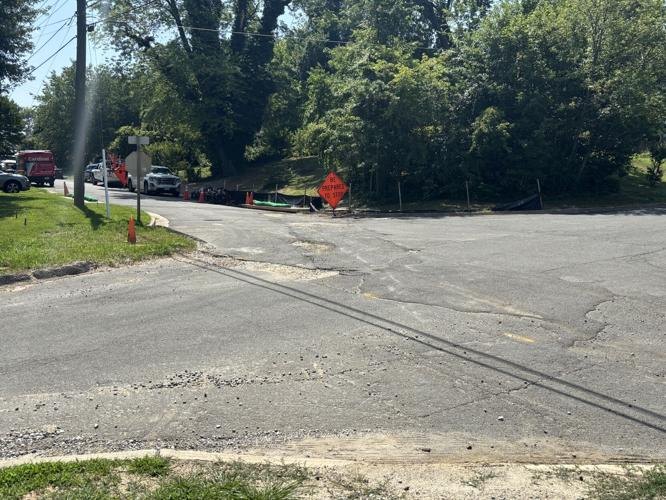 Deteriorated road intersection with cracked pavement, orange construction signs, and traffic cones.