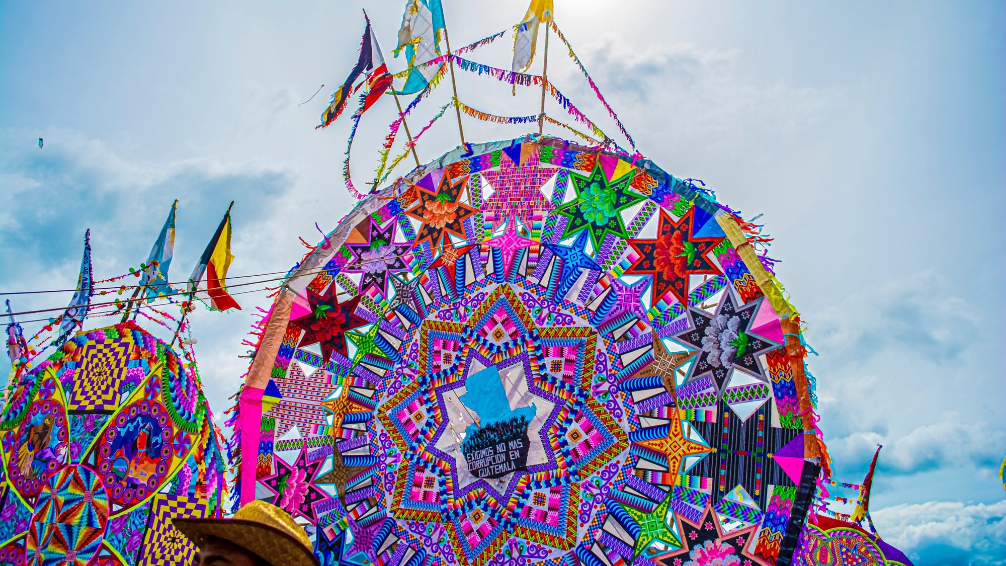 Large colorful circular giant kites with geometric patterns and streamers displayed outdoors against a cloudy sky.