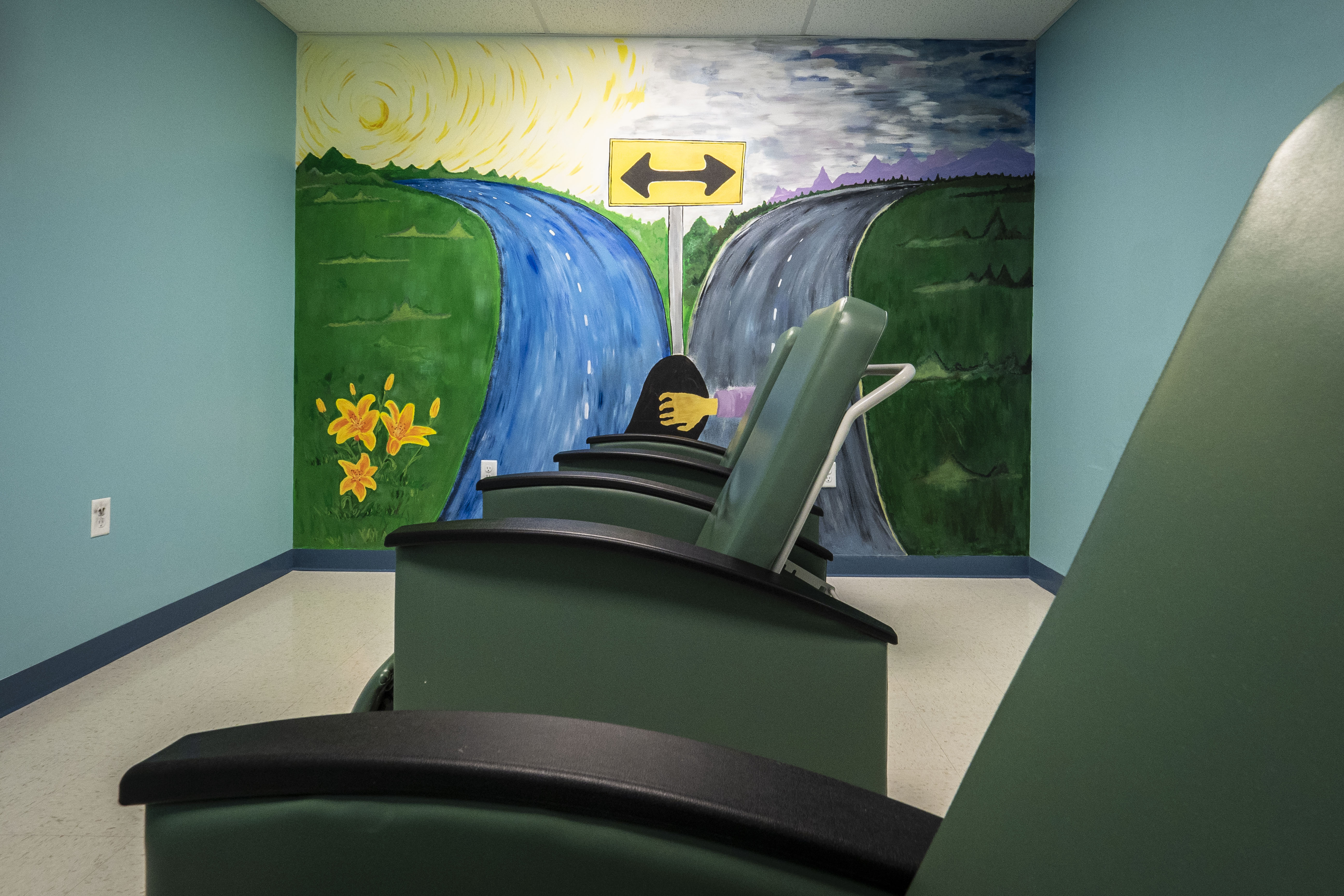 Green reclining chairs arranged in a clinical room with a colorful mural on the wall.
