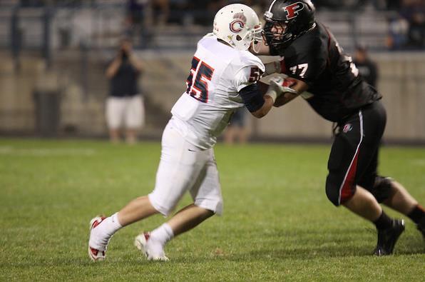 Two high school football players in opposing uniforms collide on the field during a game.