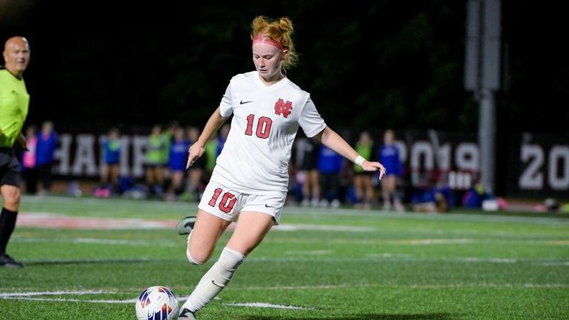 Female soccer player in white number 10 jersey preparing to kick a ball under stadium lights.