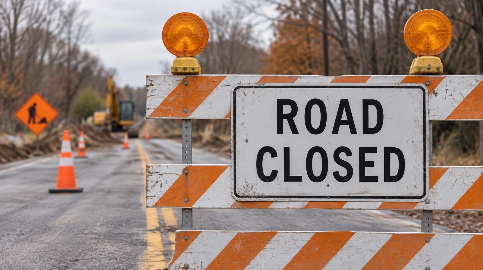 Orange road-closed barricade with flashing amber lights blocking a rural two-lane road.