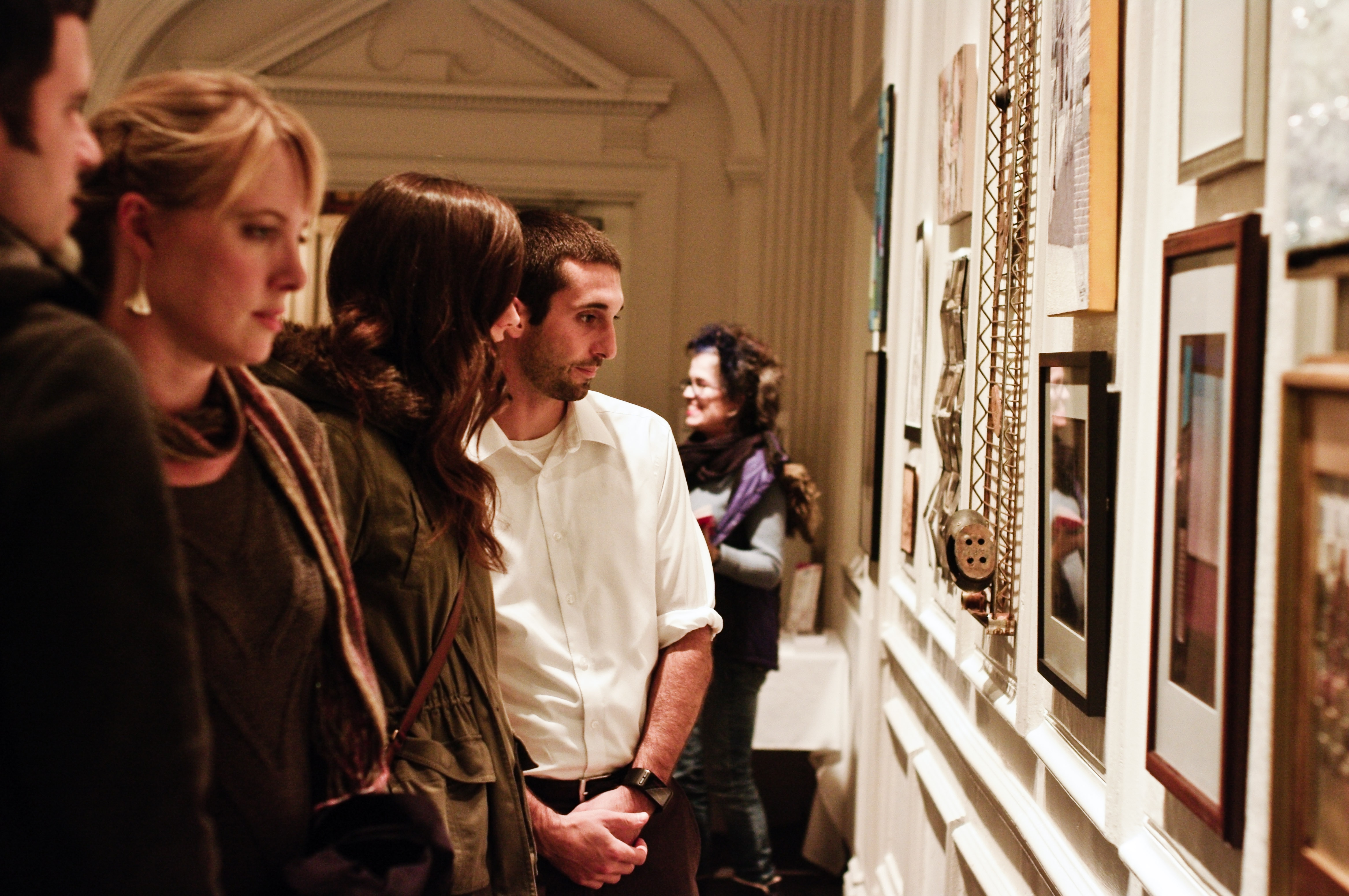 Visitors viewing framed artwork on a white gallery wall at an exhibition opening.