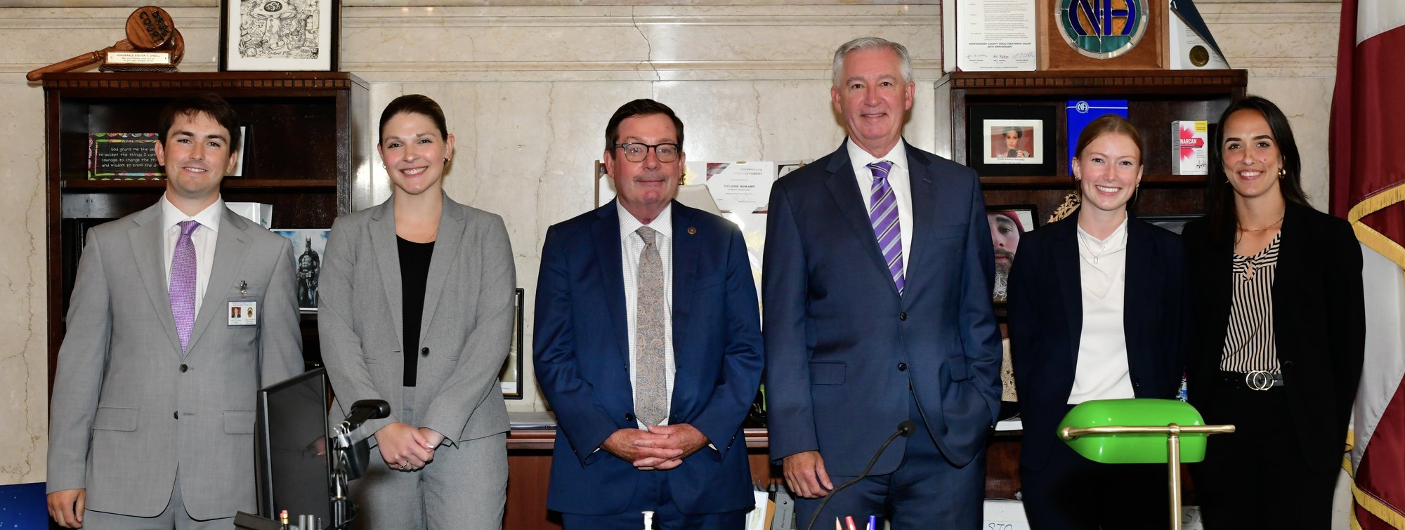 Six people in professional attire pose in a wood-paneled office.