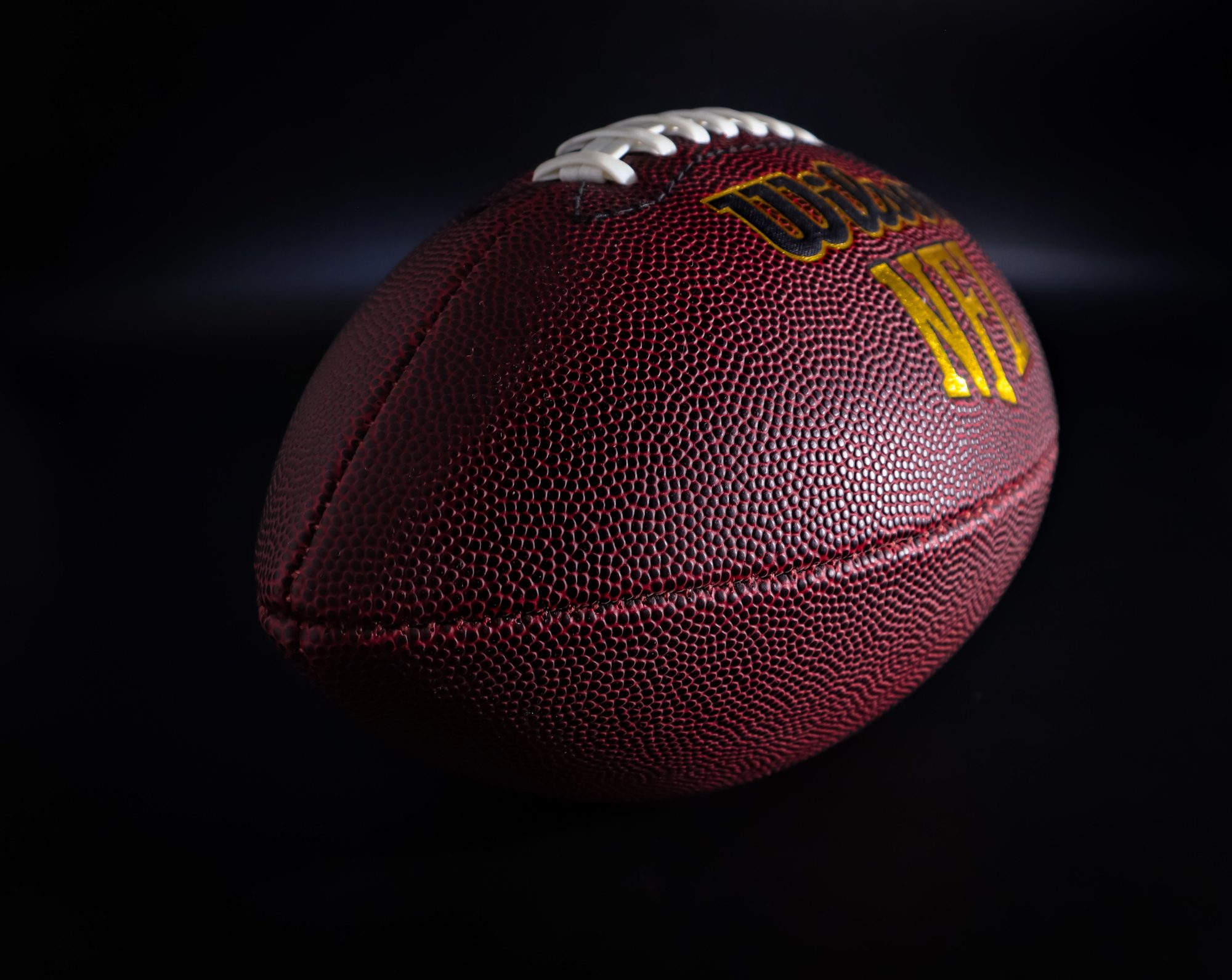 Detailed view of a traditional brown and white American football against a dark backdrop, highlighting texture.