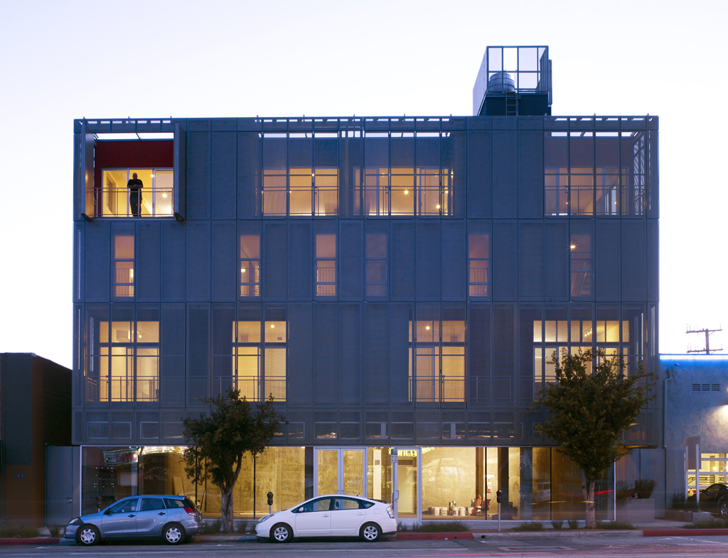 Modern multi-story mixed-use building with lit windows photographed at dusk on a city street.