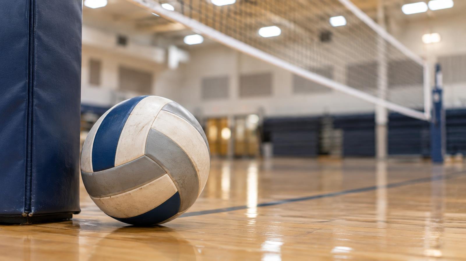 A volleyball resting on a hardwood gymnasium floor near the net post.