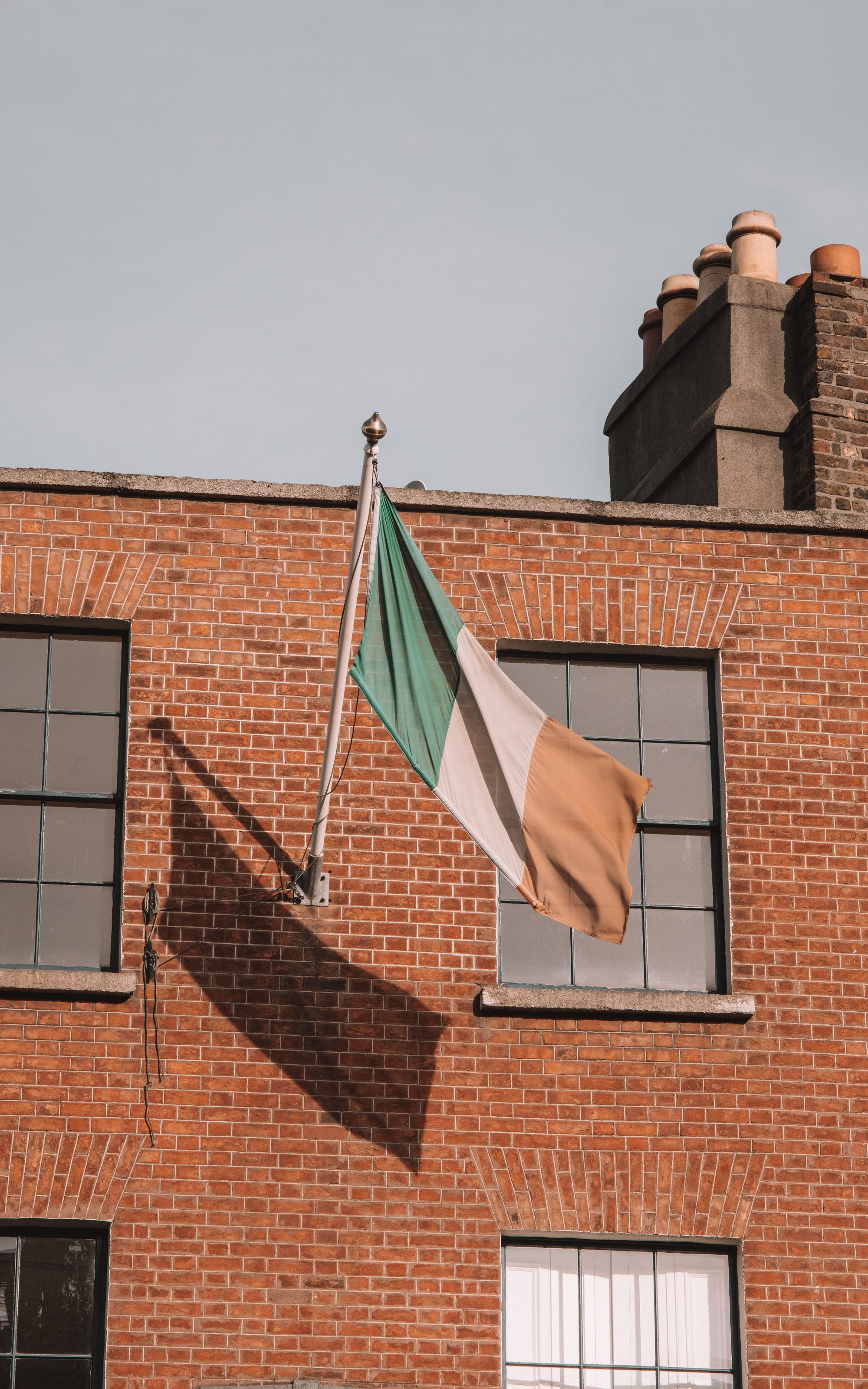The Irish flag waves on a brick building facade in Dublin, Ireland.