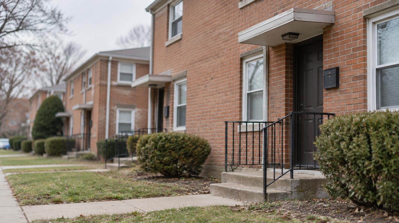 A row of brick apartment buildings with small front yards and concrete walkways.