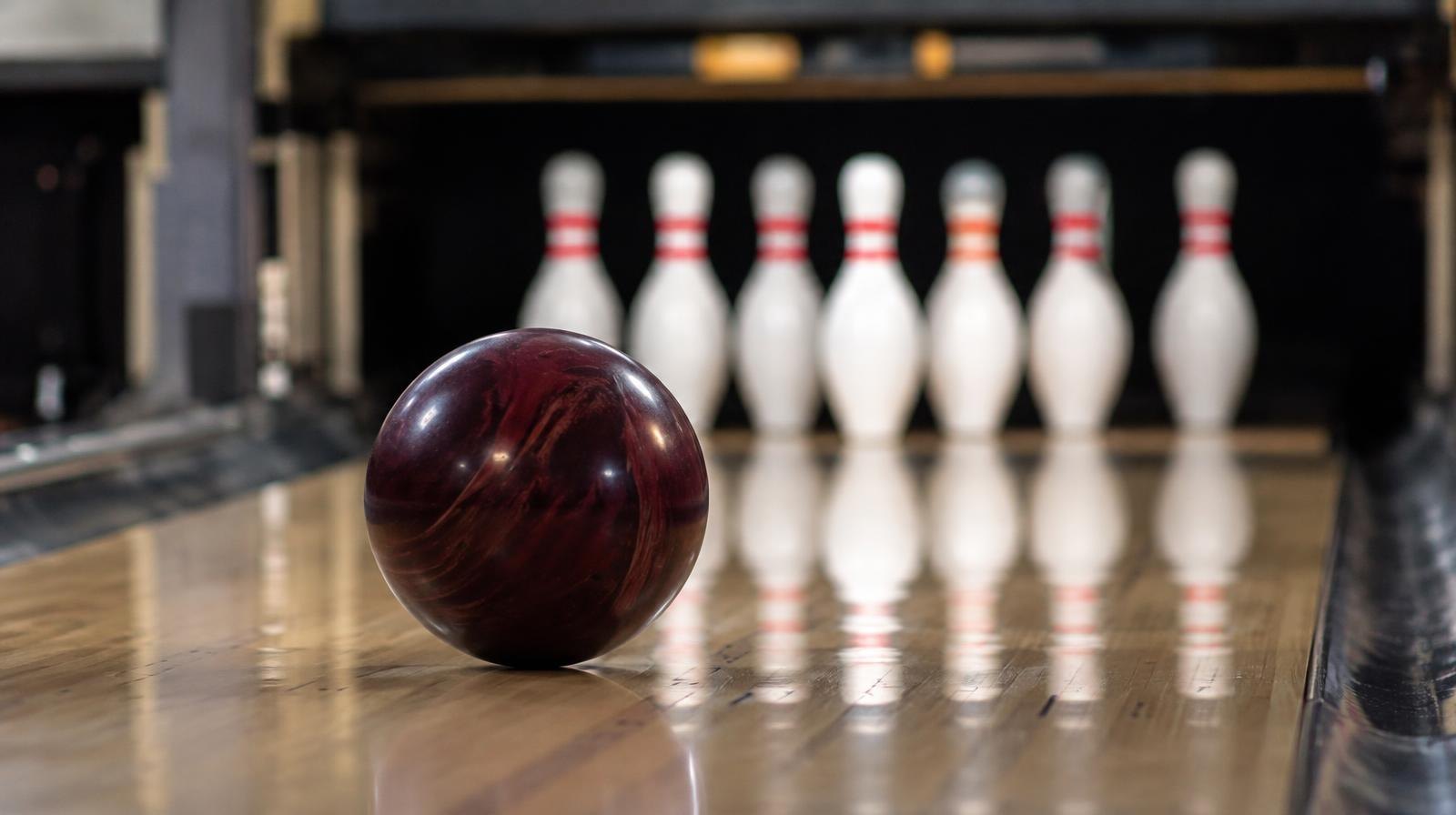 A bowling ball rolling down a hardwood lane toward ten white pins.
