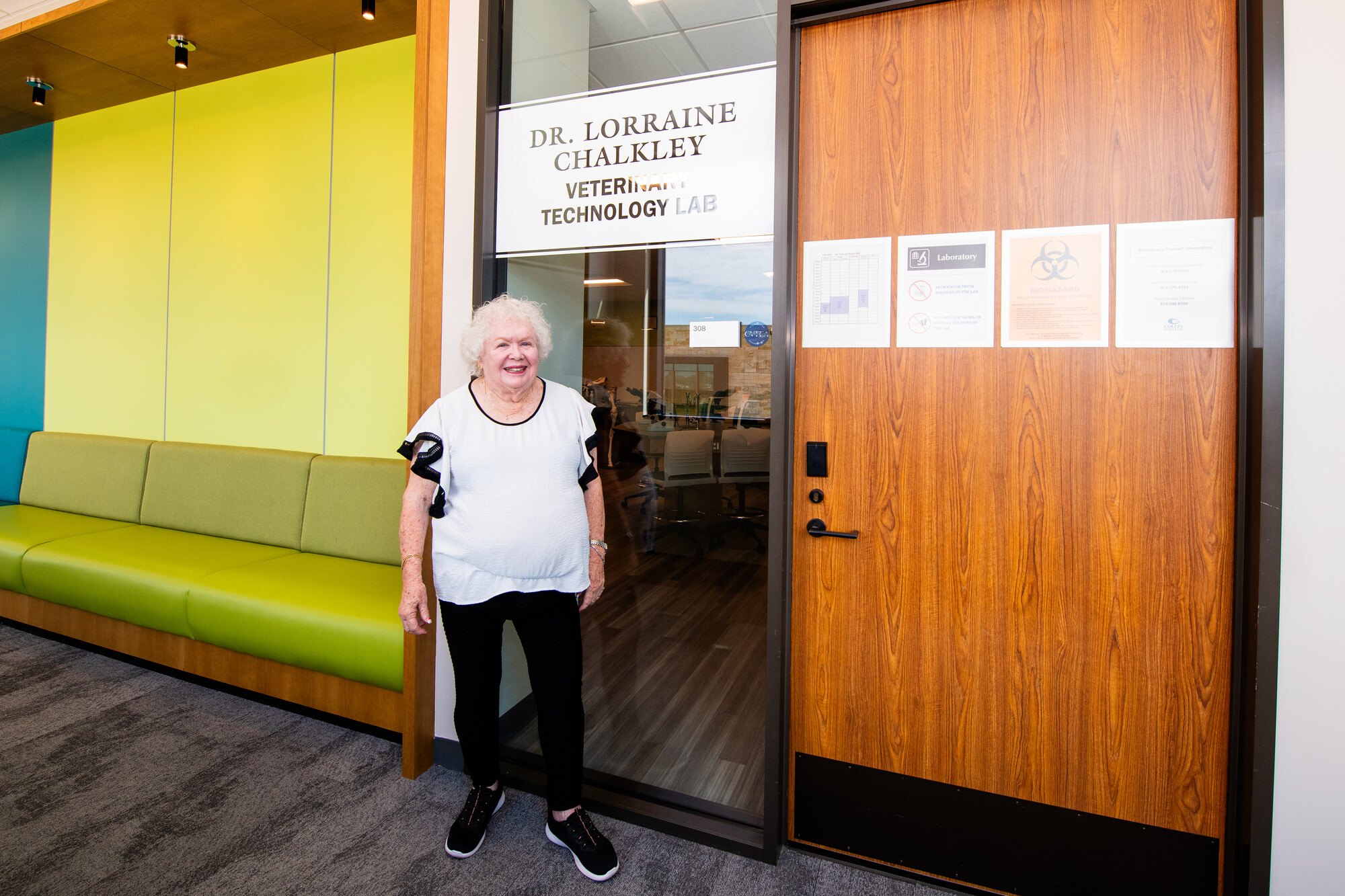 Woman in white top standing before a door labeled with a veterinary technology lab name.