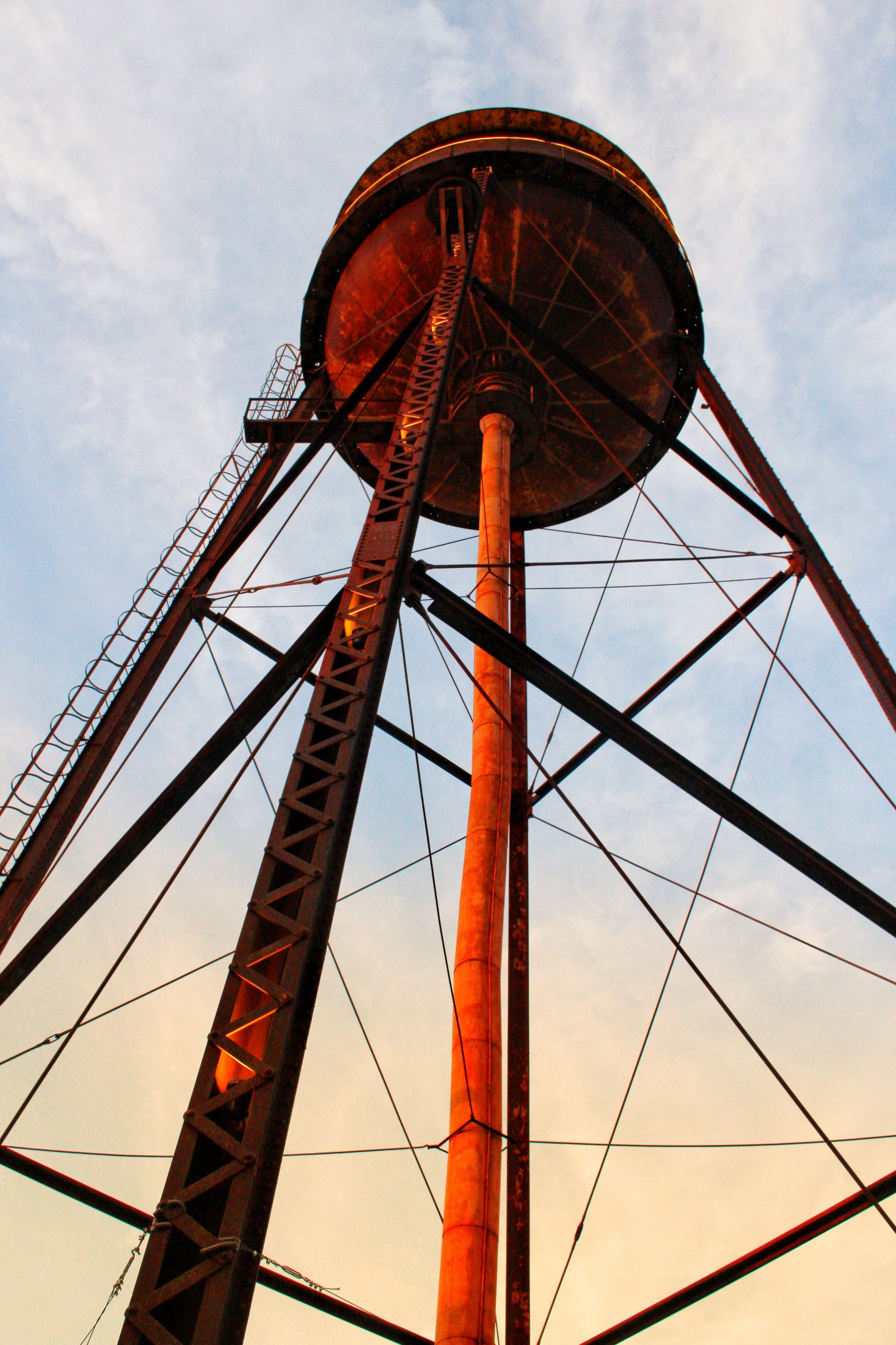 Low angle view of an old rusty water tower against a sunset sky.