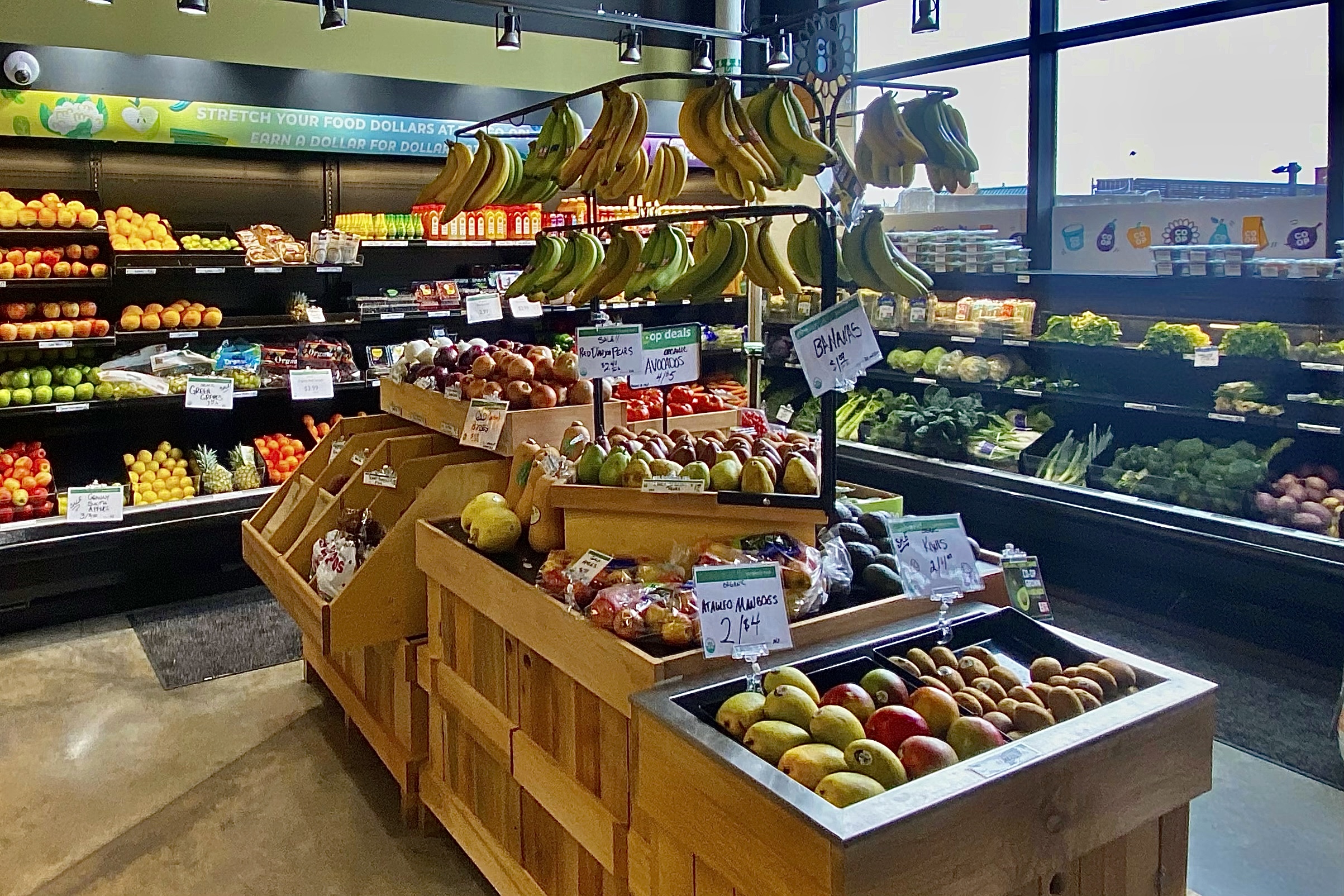 Wooden tiered display stand stocked with fresh fruit inside a food cooperative.