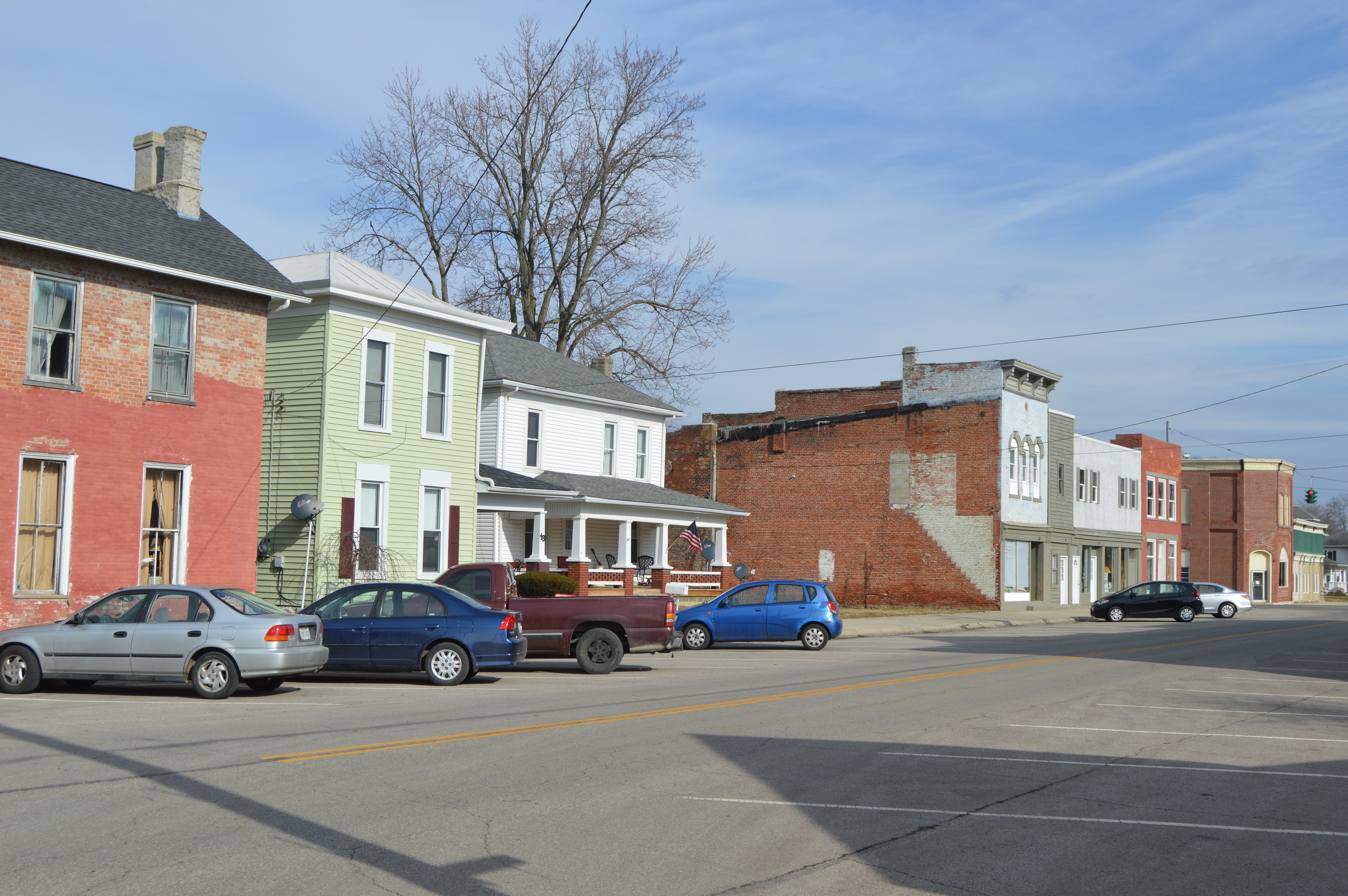 Row of brick storefronts along a downtown street with cars parked at the curb.