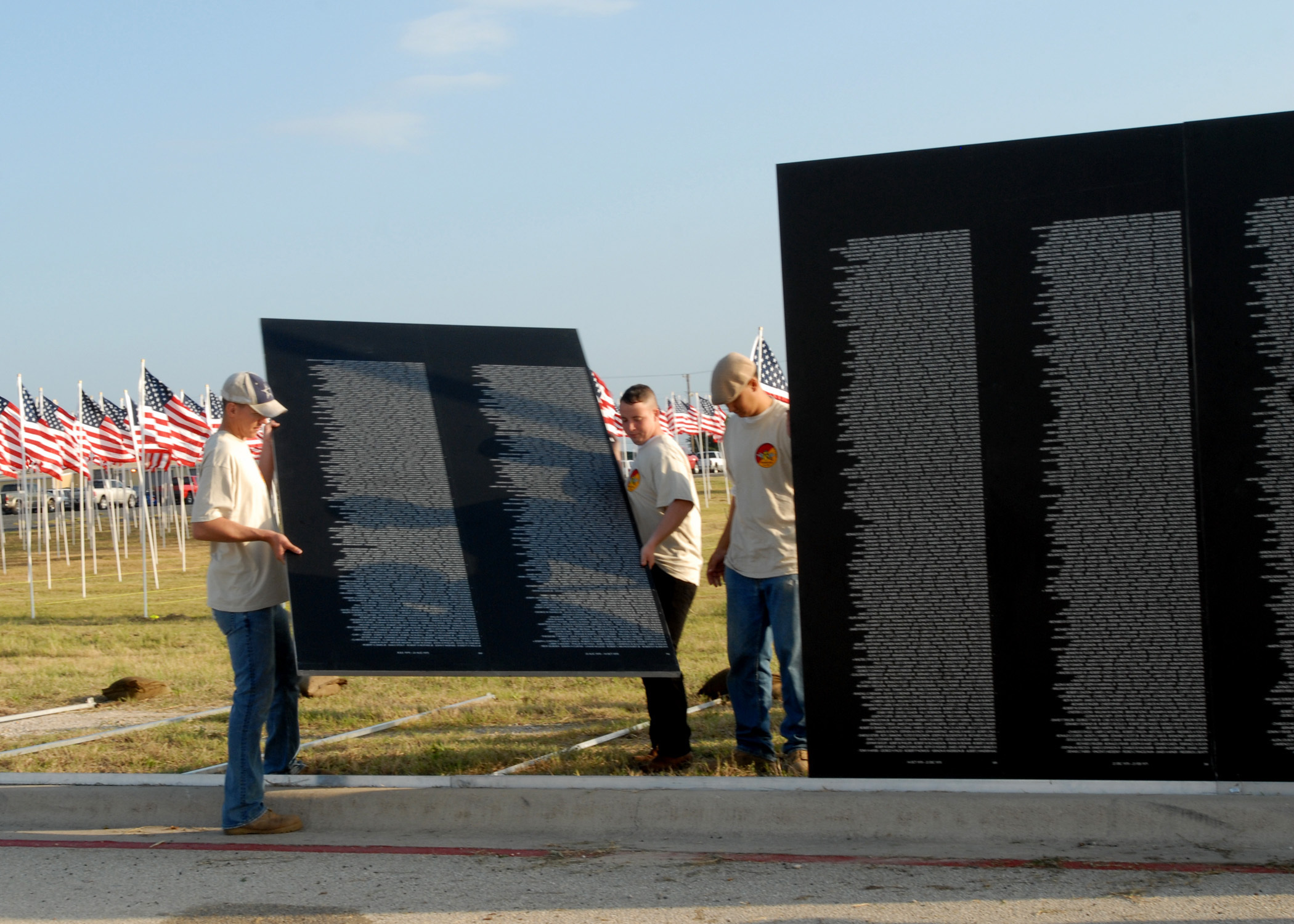 Workers carry large black name-engraved memorial panels with rows of American flags behind them.
