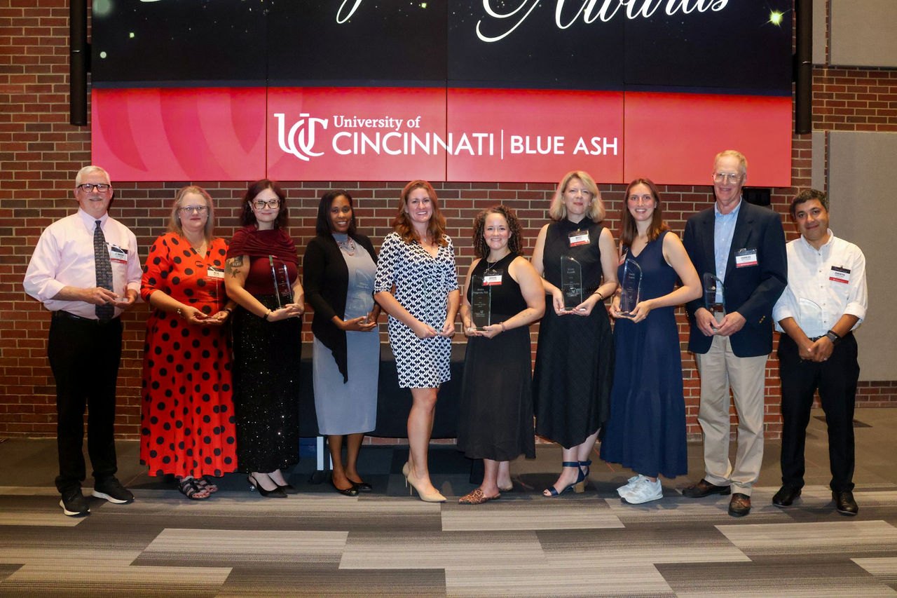 Group of award recipients holding glass trophies in front of a branded backdrop.