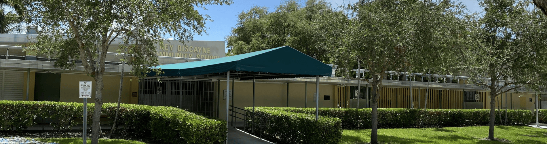 Key Biscayne K-8 Center entrance with a green shade canopy, trees and school sign.