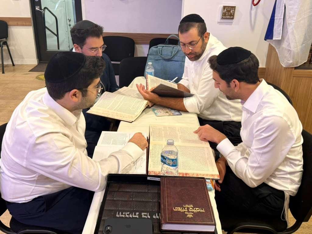 Four young men wearing kippot seated around a table with open religious books.