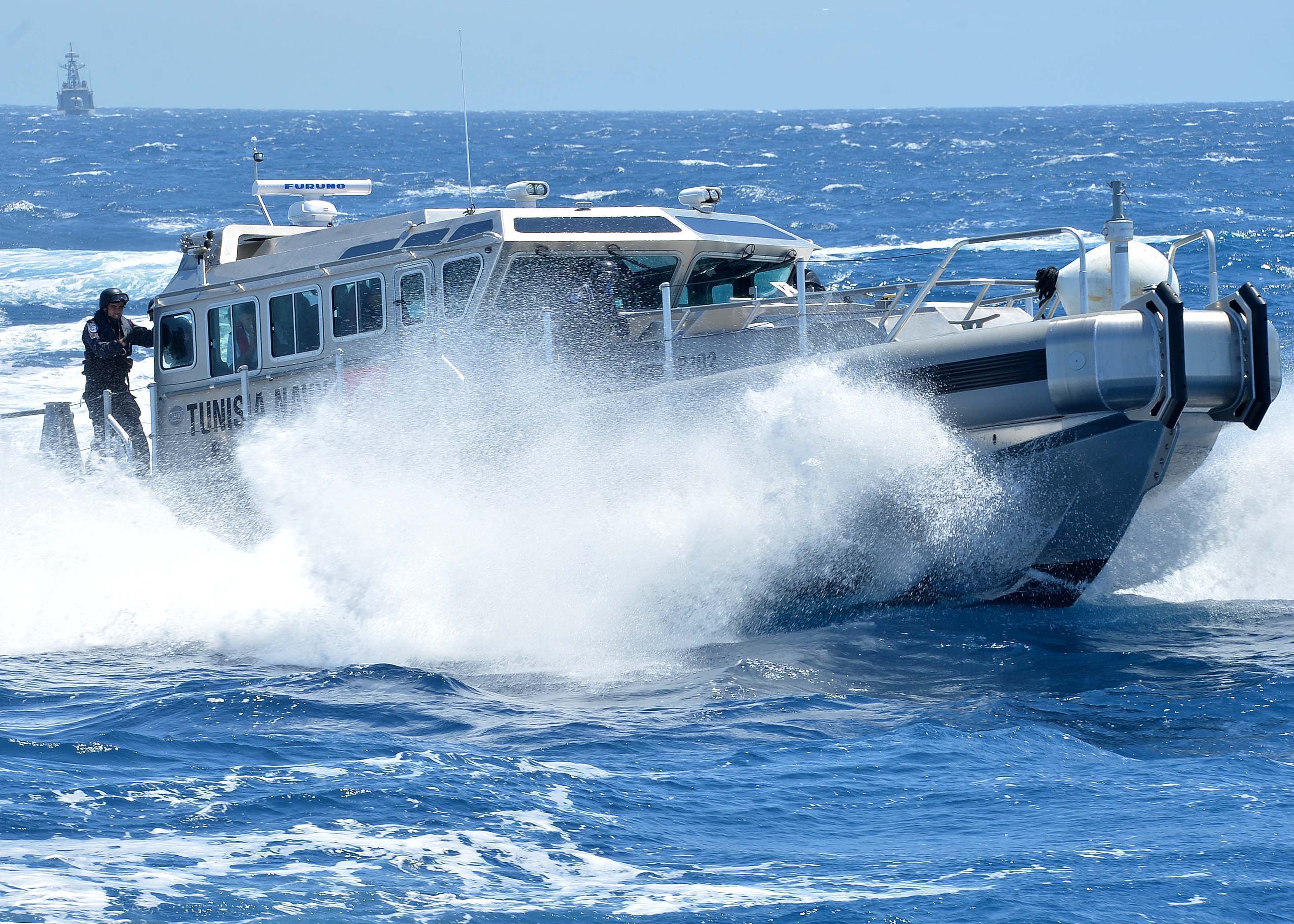 A fast military patrol boat cutting through open ocean water at high speed.