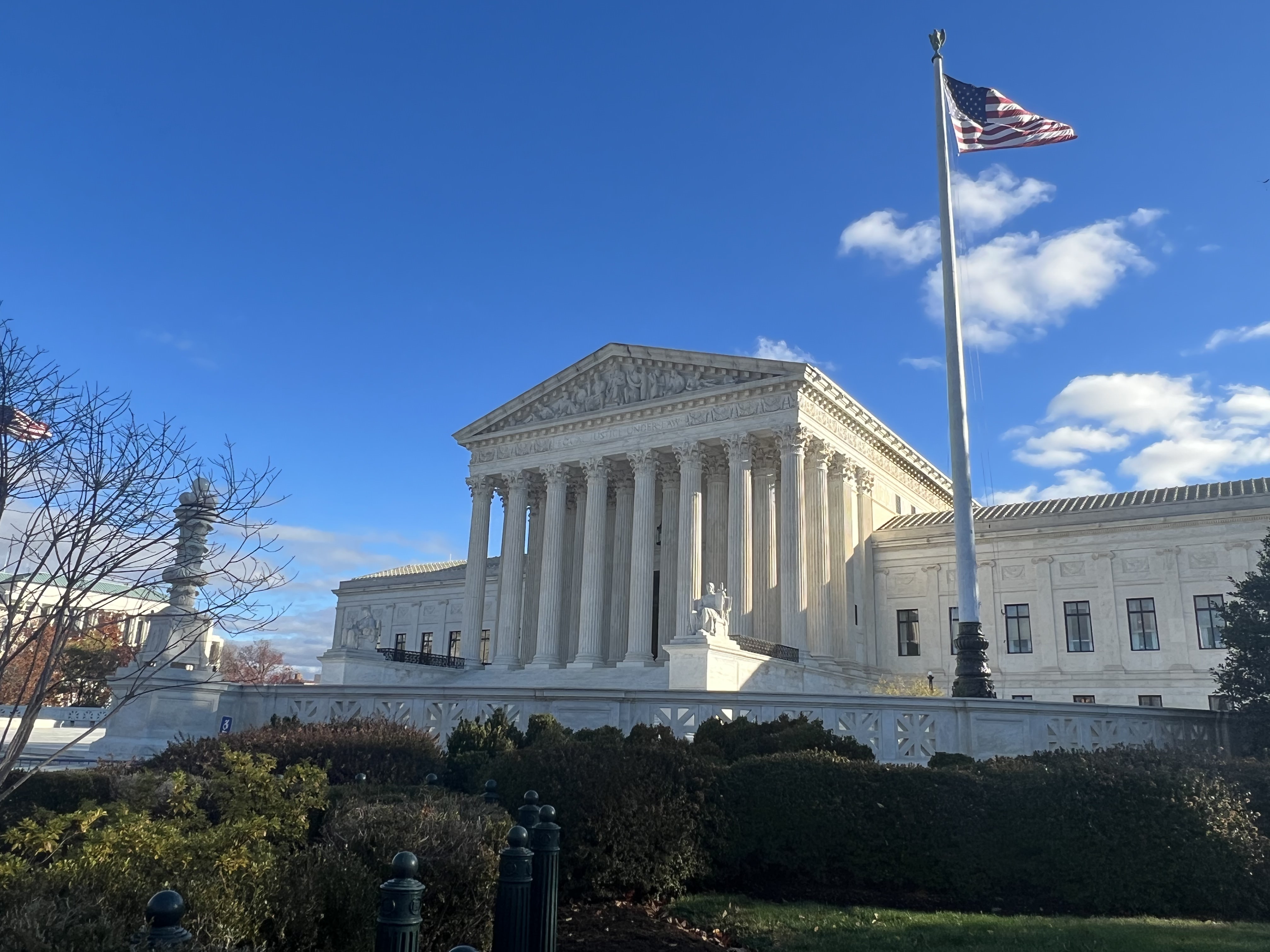 The United States Supreme Court building on a clear day with an American flag on a tall flagpole.